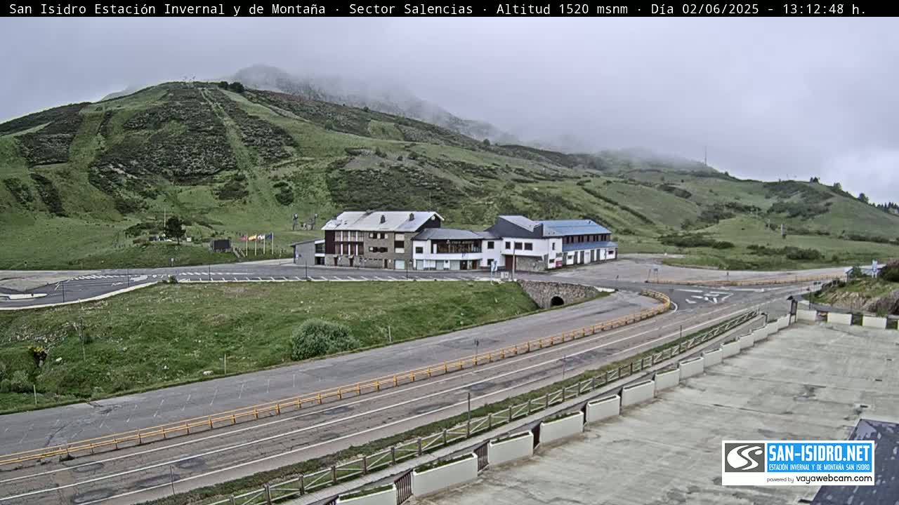 A mountainside with a parking lot, several buildings, and roads, under overcast skies.