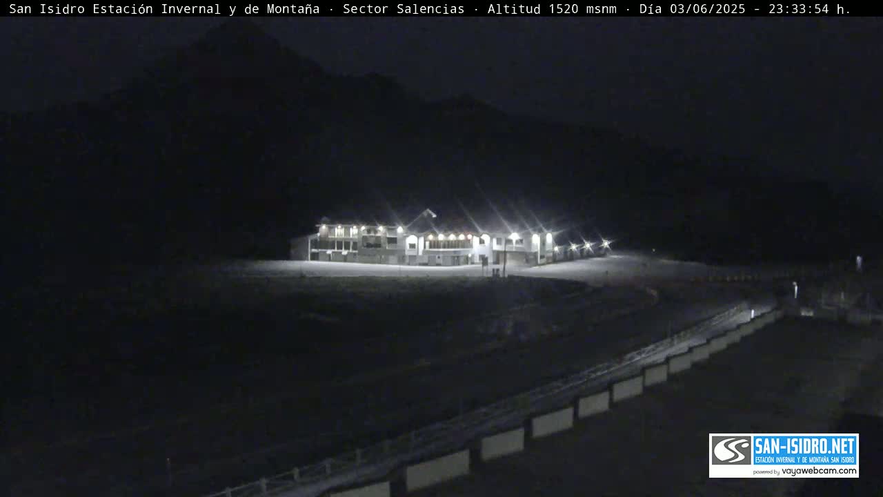 A brightly lit building sits on a snow-covered landscape at night, with a dark mountain in the background.