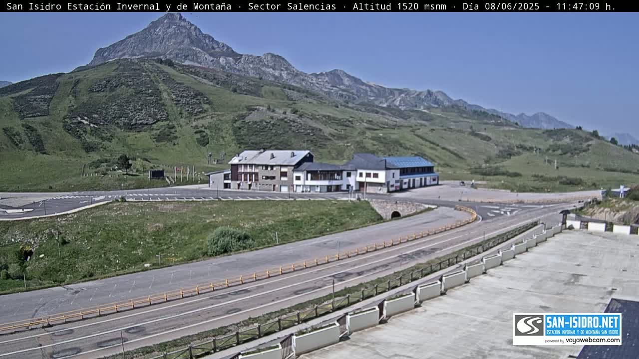 A mountainside parking lot with a long road and several buildings is visible on a sunny day.