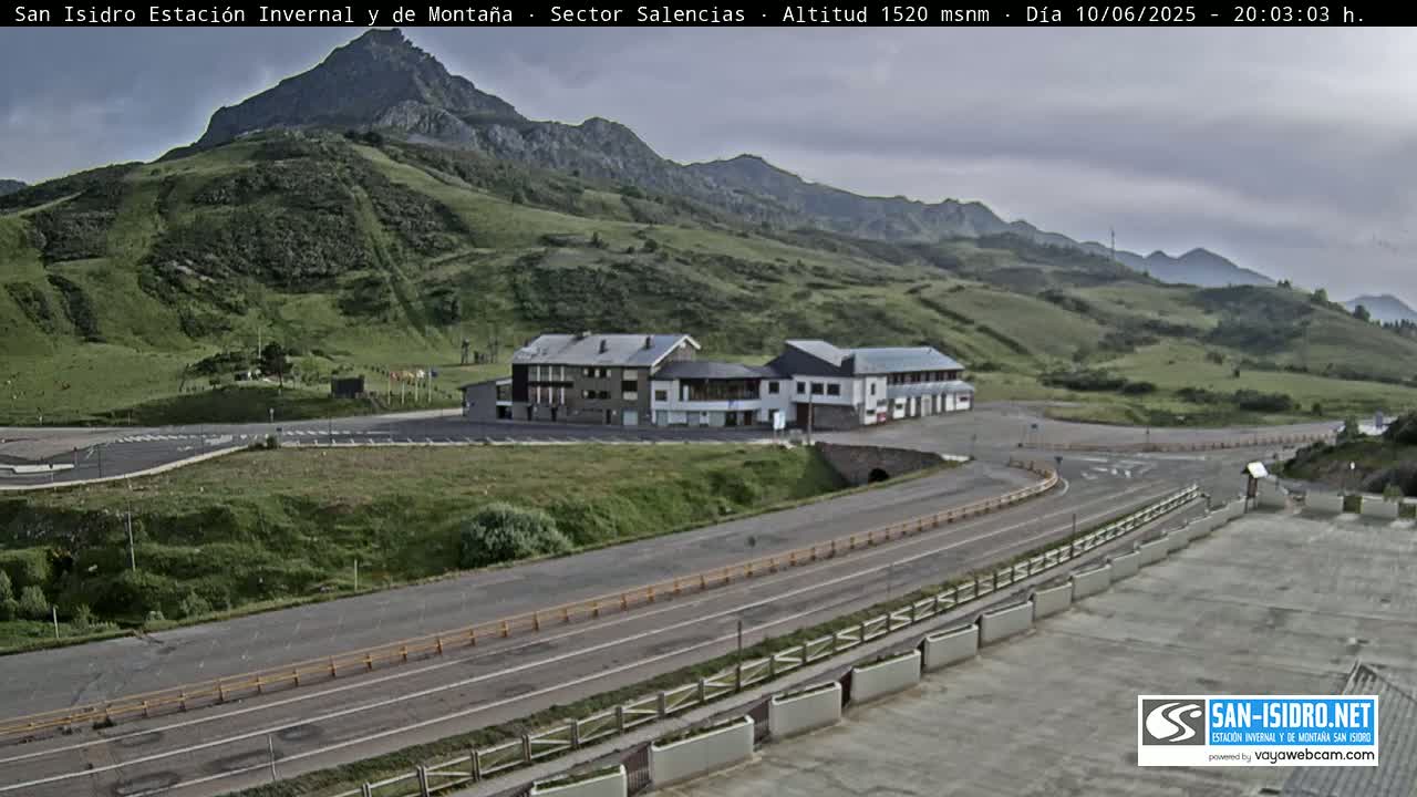 A mountainside parking lot with a building complex and a winding road under an overcast sky.