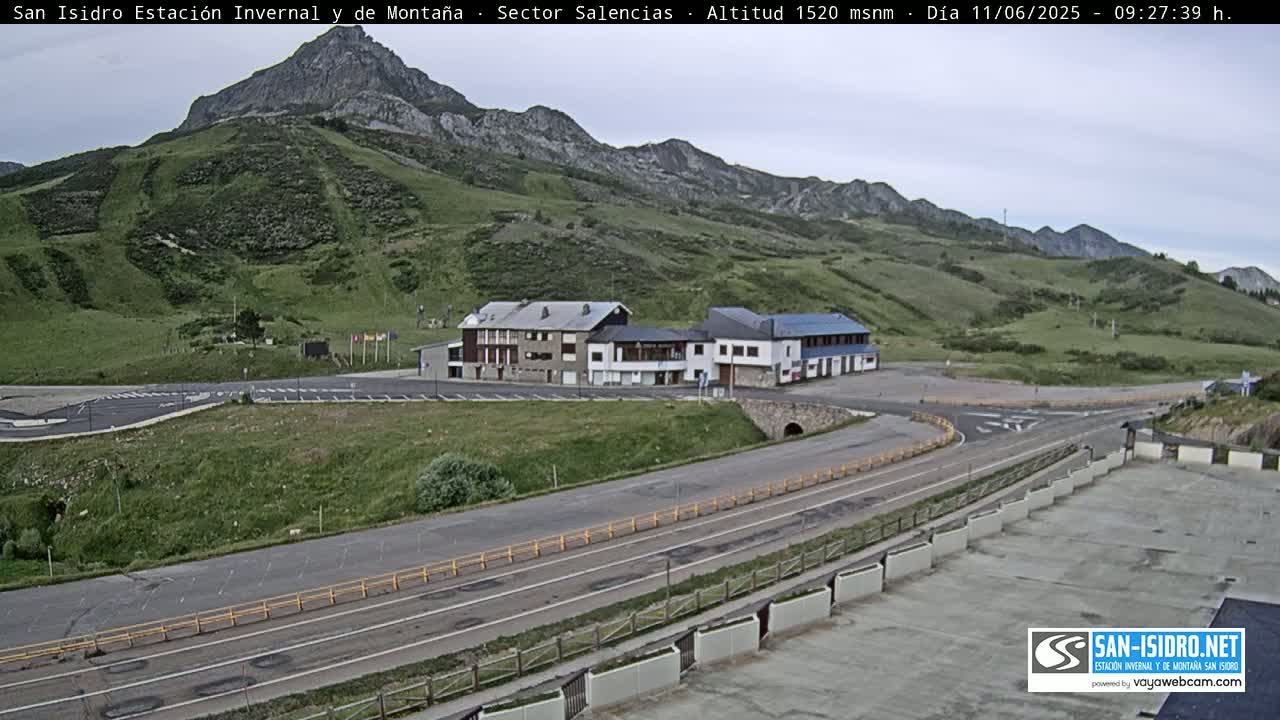 A mountainside resort with a parking lot and buildings is seen under partly cloudy skies.