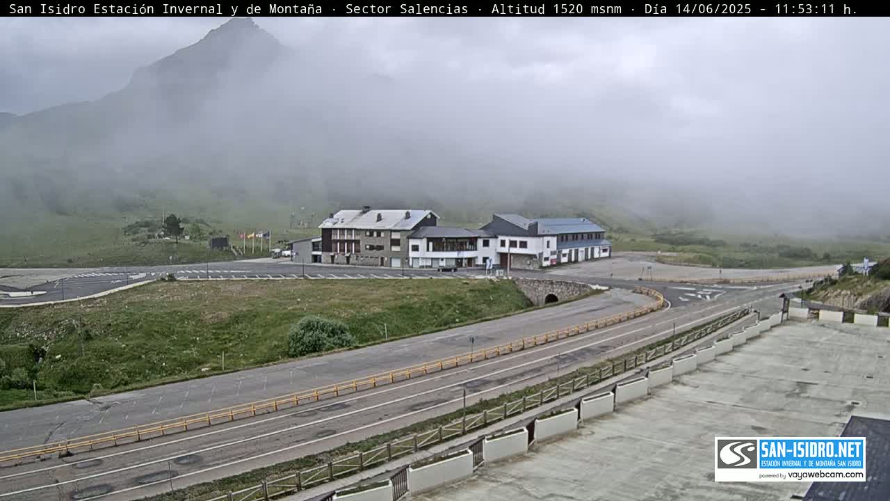 A foggy mountain vista reveals a roadway curving past a cluster of buildings and parking areas.