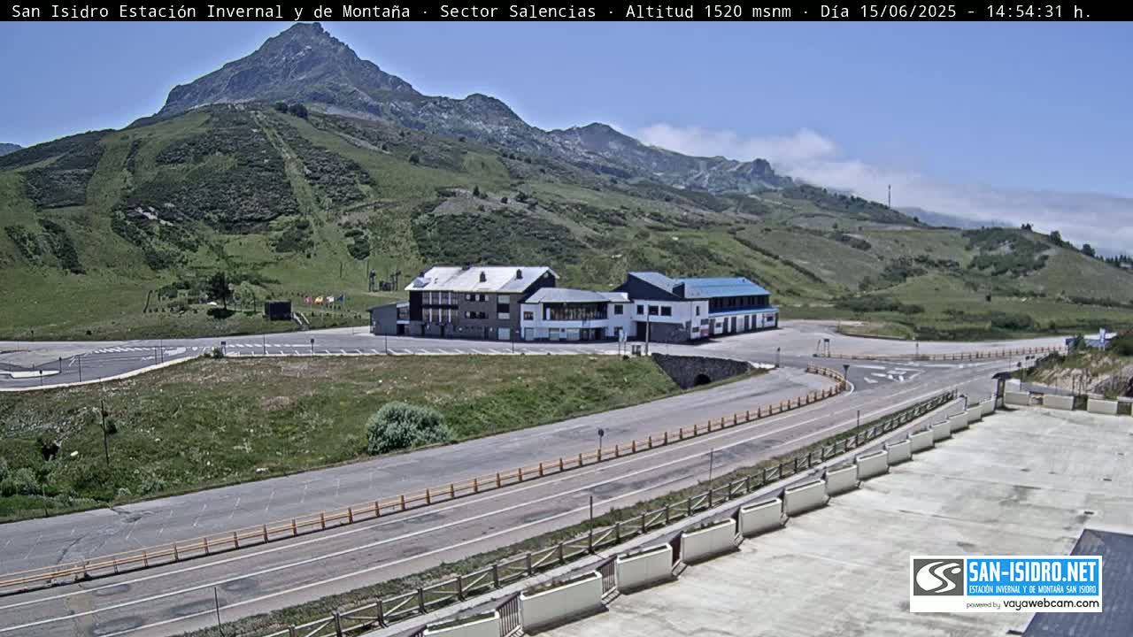 A mountainside parking lot and road with a building complex, under a mostly clear sky with some high clouds.
