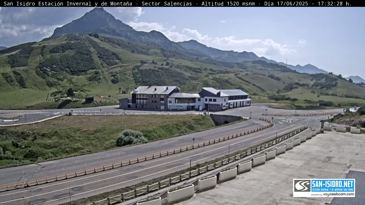 A mountainside building complex with parking lots and roads is visible under partly cloudy skies.