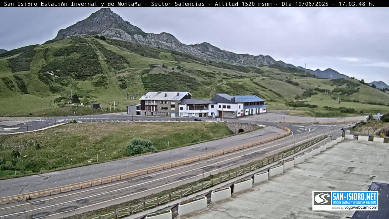 A mountaintop parking area with several buildings, roads, and green hills under an overcast sky.