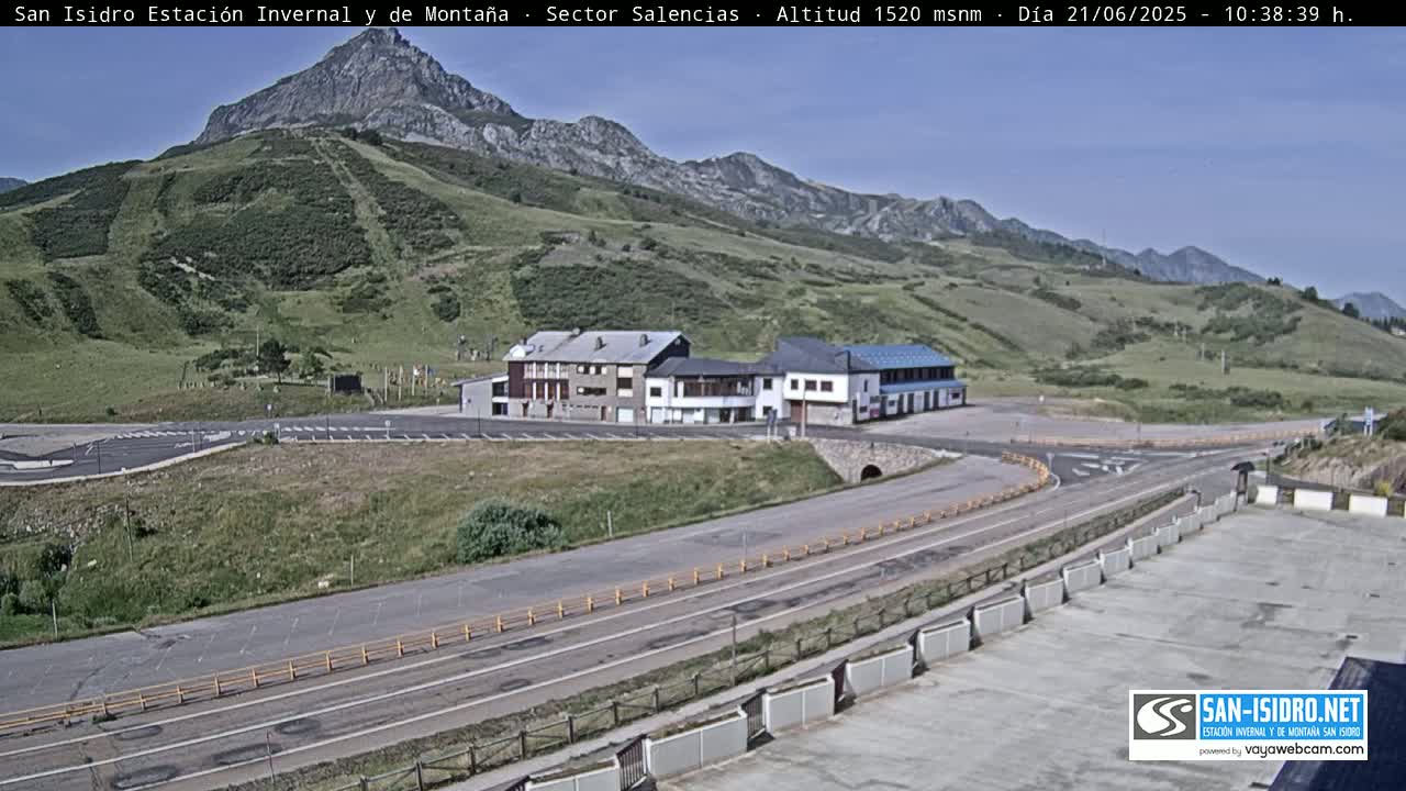 A mountainside resort with a parking lot and roadway is visible under a clear, sunny sky.