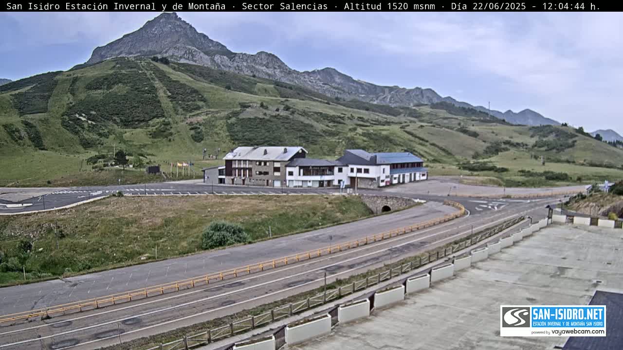 A mountainside parking lot and road curves around a complex of buildings under a partly cloudy sky.