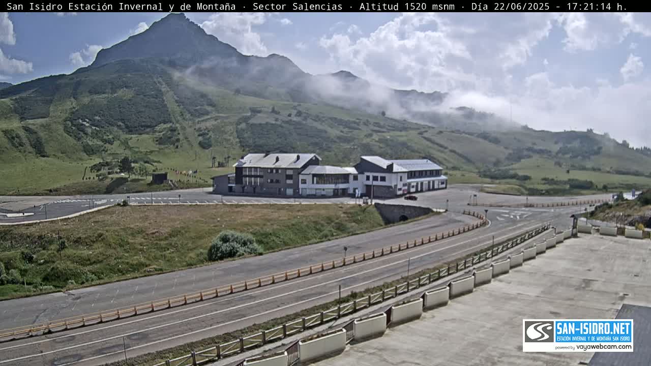 A partly cloudy day reveals a mountainside with a building complex and roads near the base, partially obscured by fog.
