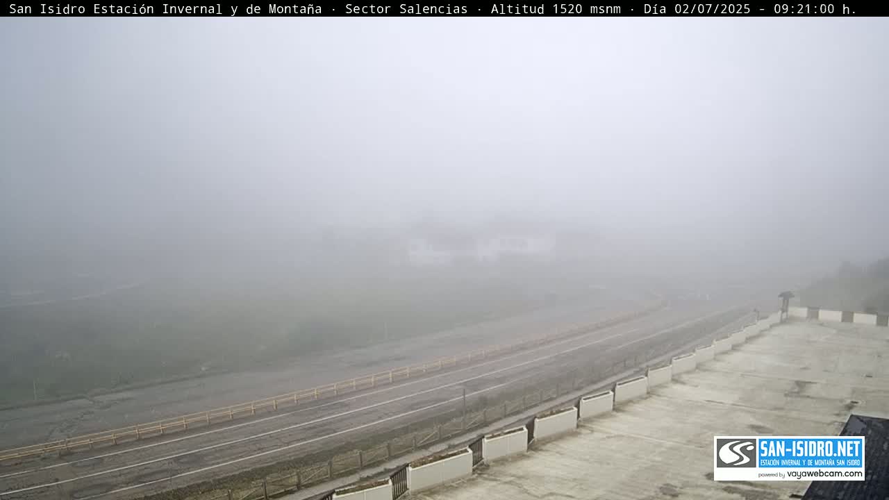 A foggy view of a multi-lane road and a parking lot, observed from an elevated position.