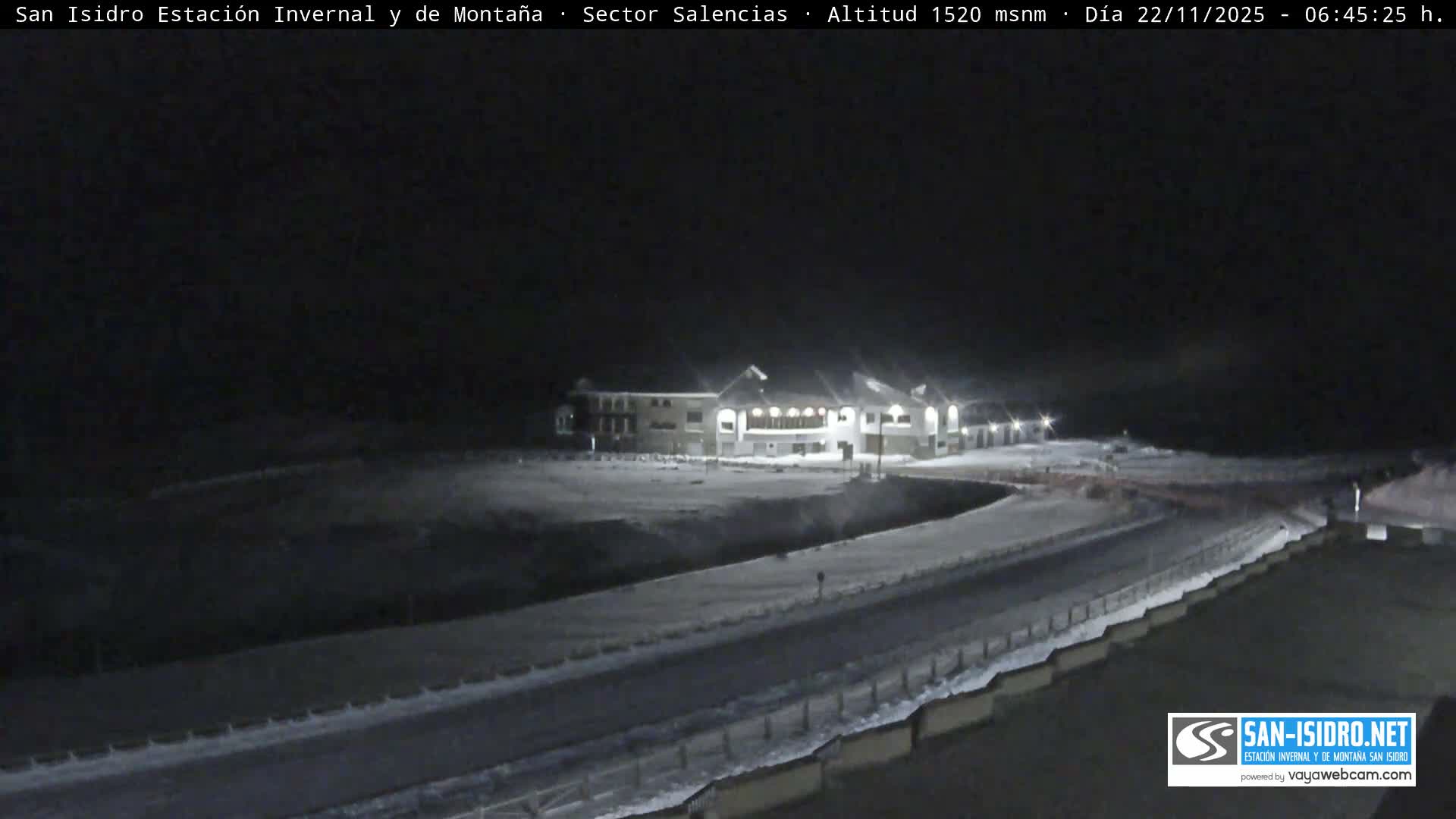 Under a clear, dark sky, an illuminated resort building stands prominently in a snow-covered winter landscape at night.