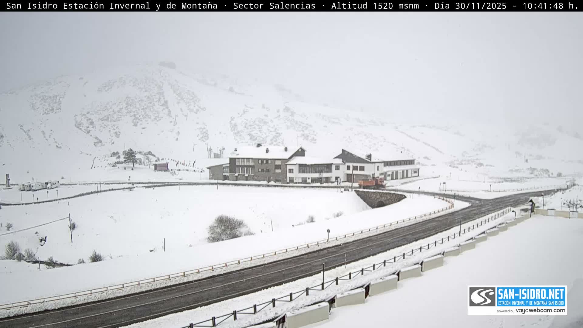 The image depicts a snow-covered mountain resort featuring a winding road and several buildings under hazy, overcast winter conditions.