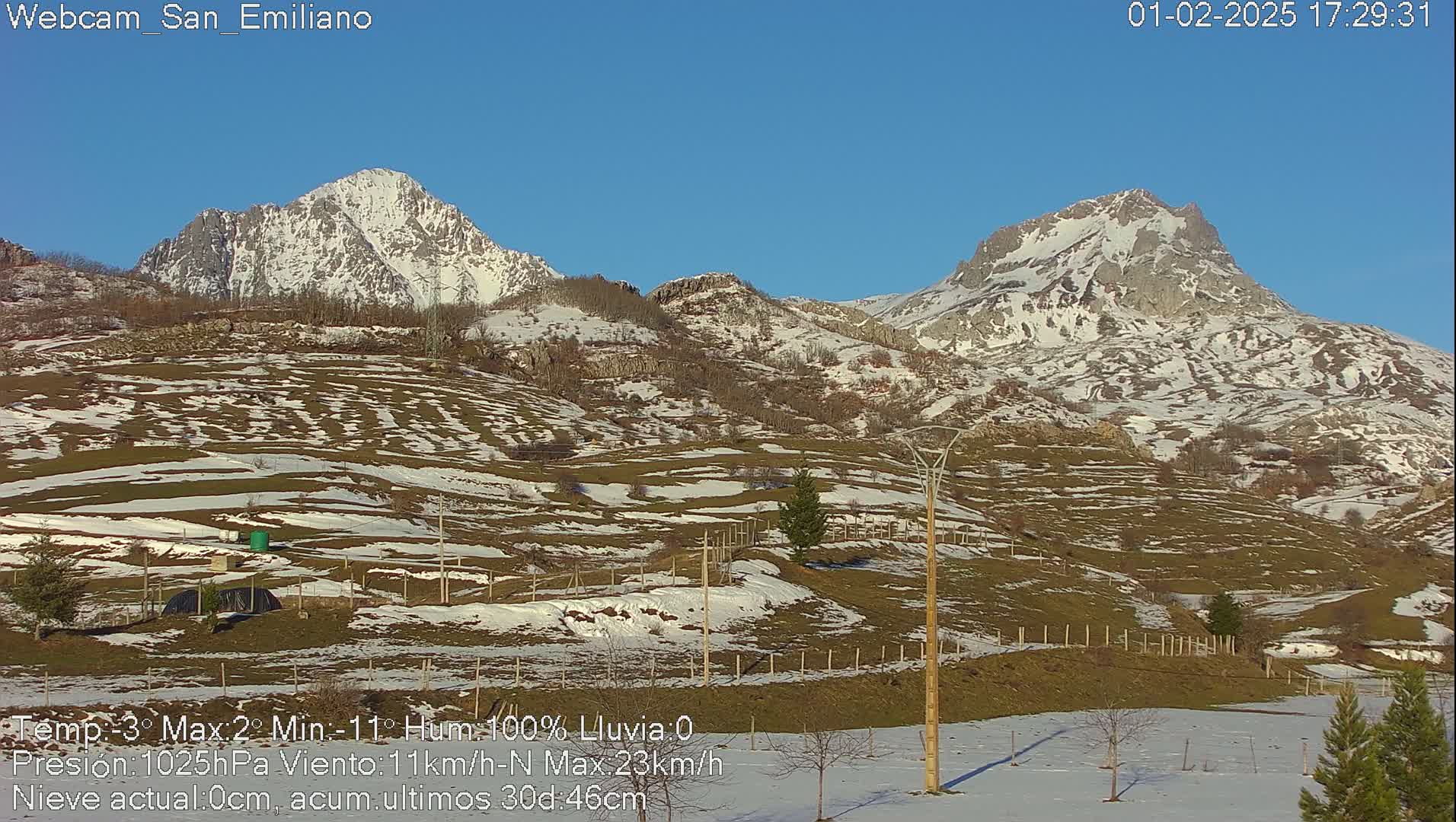 Snow-dusted hills and mountains under a clear blue sky.