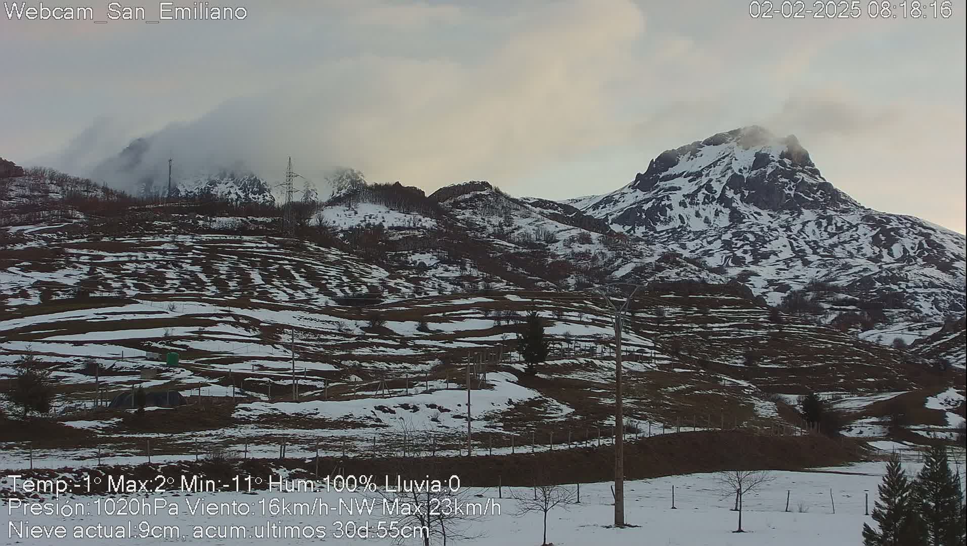 A snow-dusted mountain range is partially obscured by fog under an overcast sky.