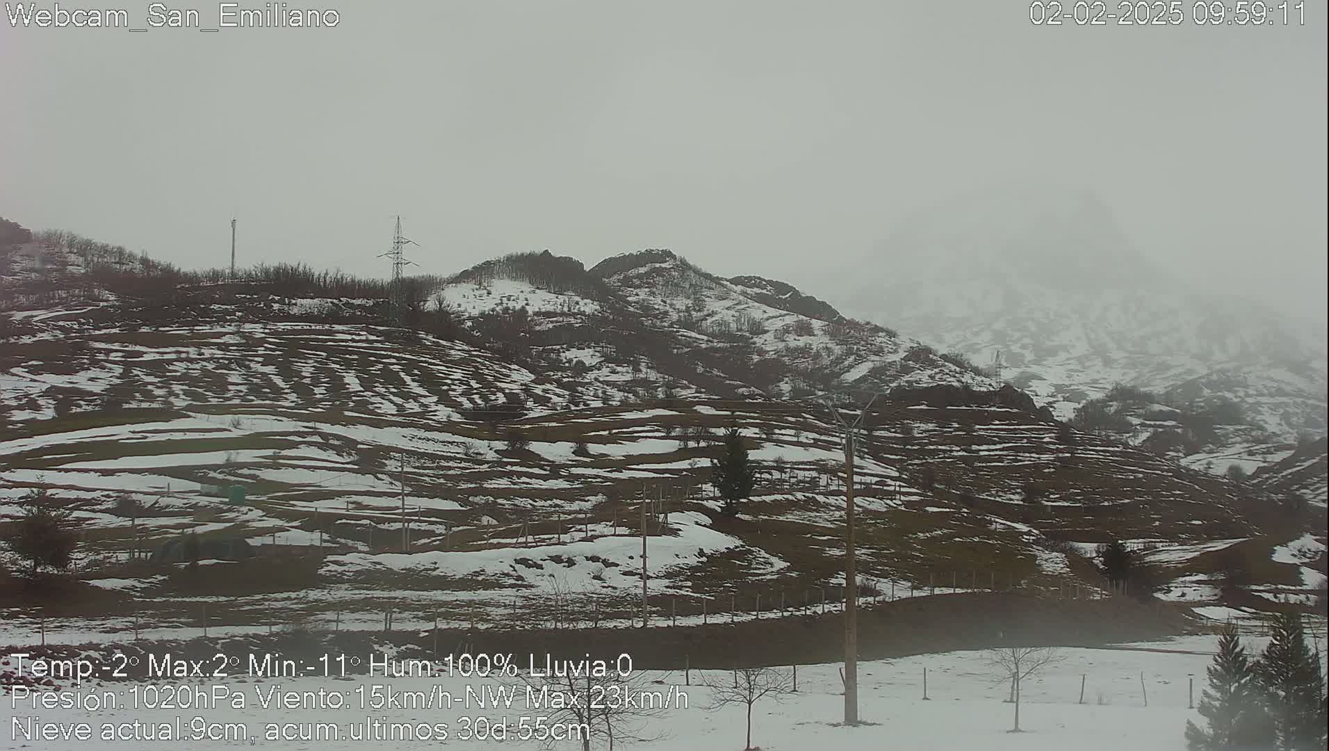 A snow-covered landscape with rolling hills and sparsely wooded areas under an overcast sky.