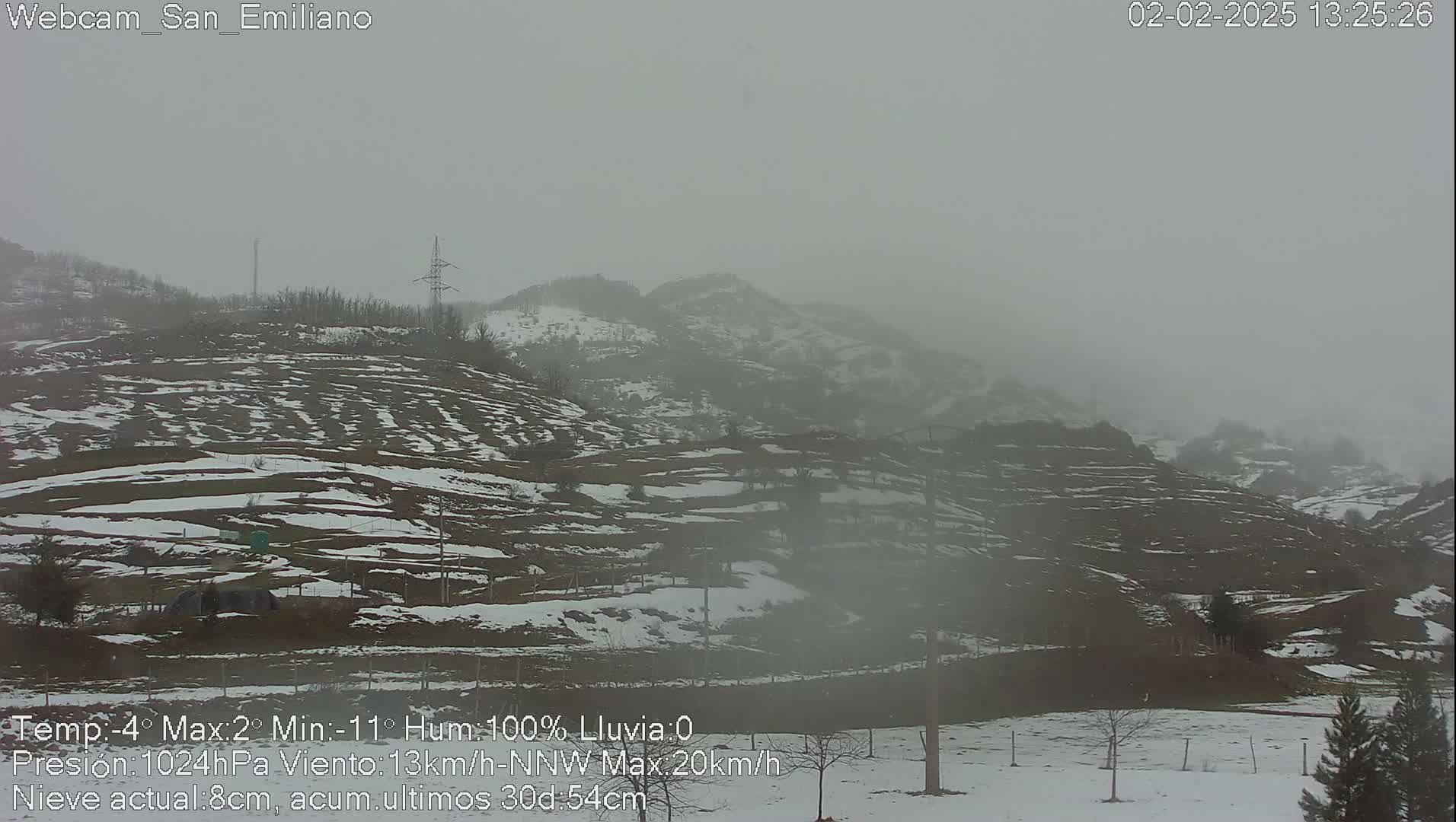 A snow-covered hilly landscape is shrouded in a thick fog.
