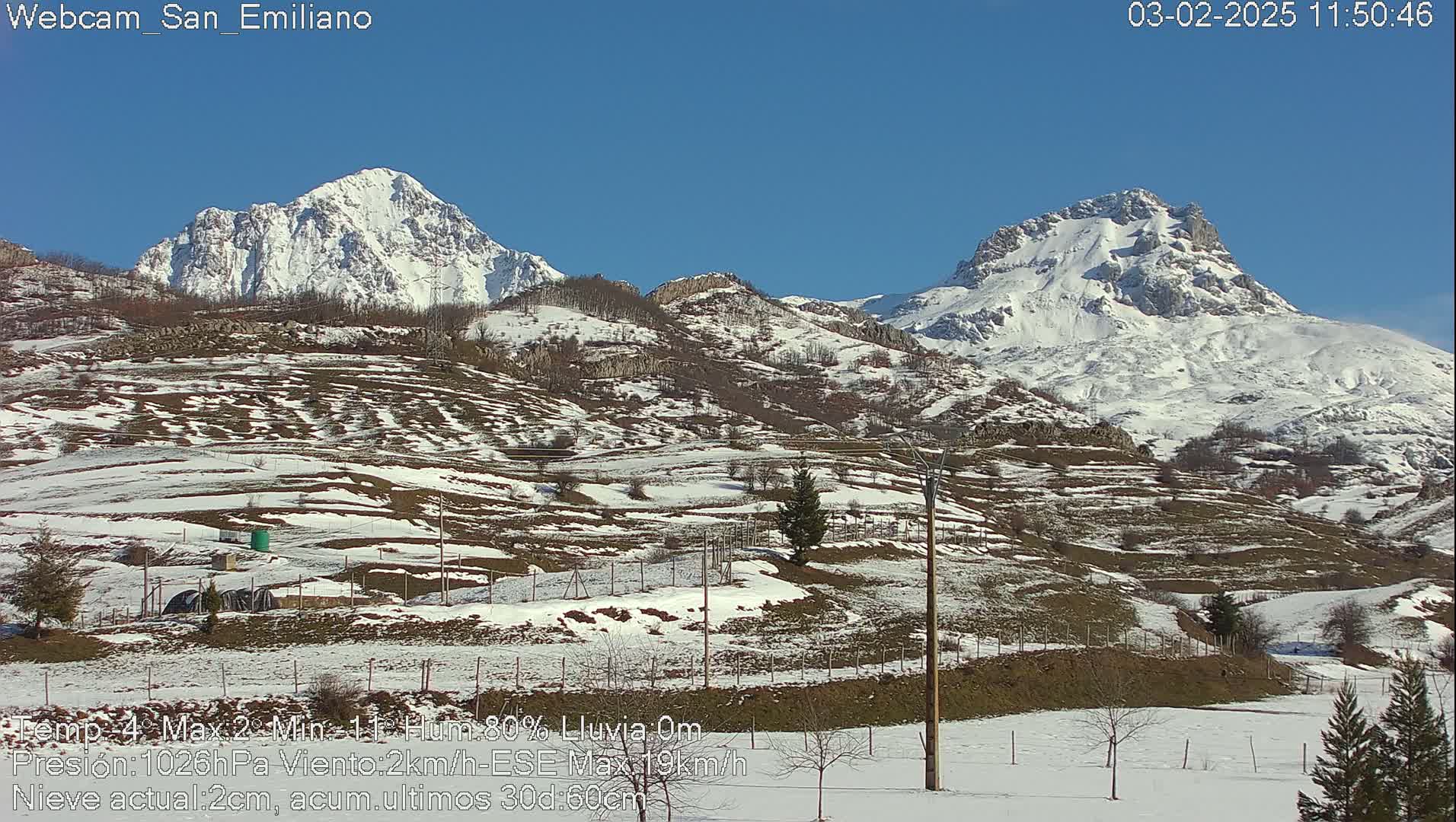 A snow-dusted landscape with two snow-capped mountains in the background under a clear blue sky.