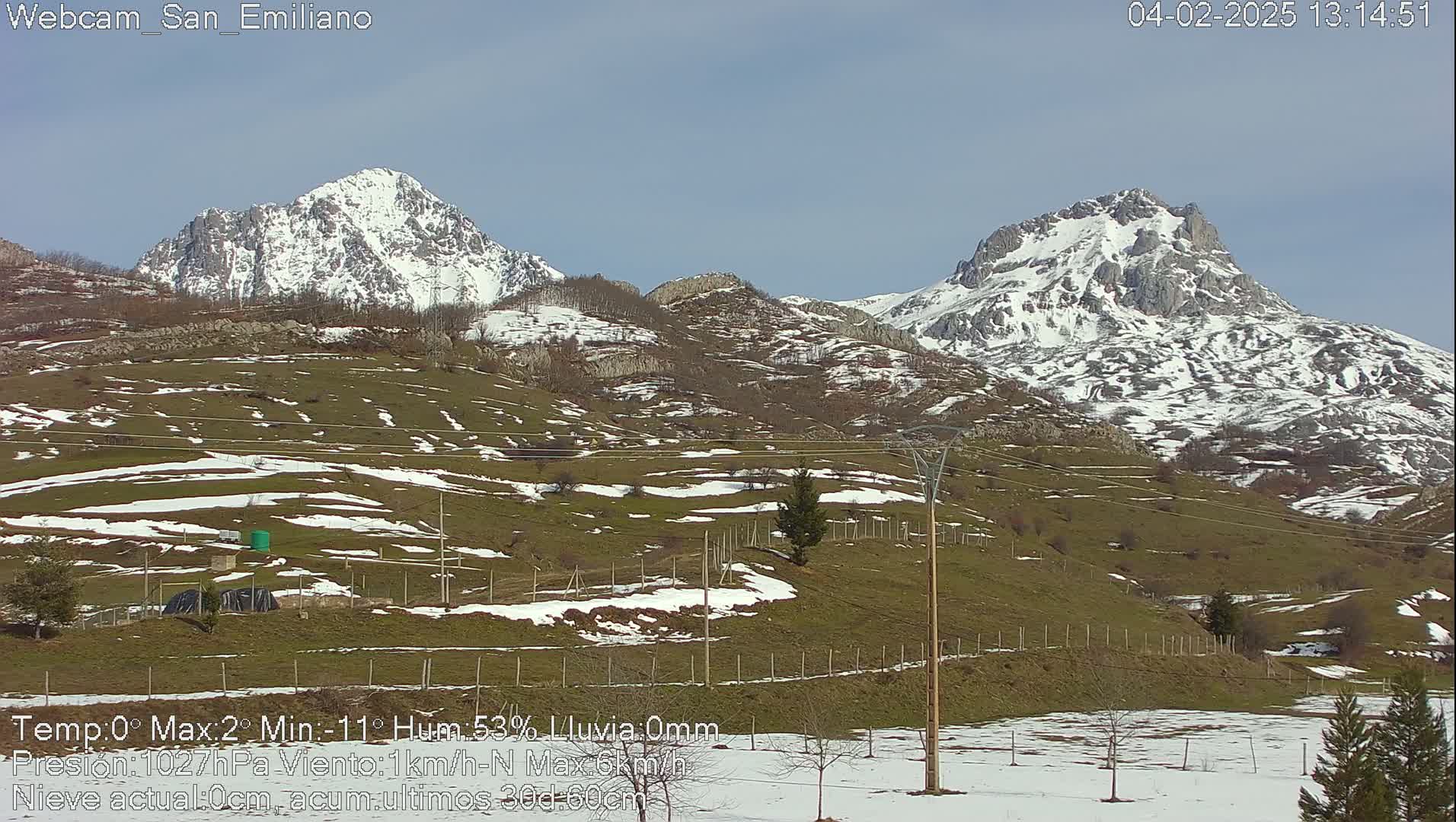 Snow-dusted, green hills and mountains with snow-capped peaks are visible under a clear, bright sky.