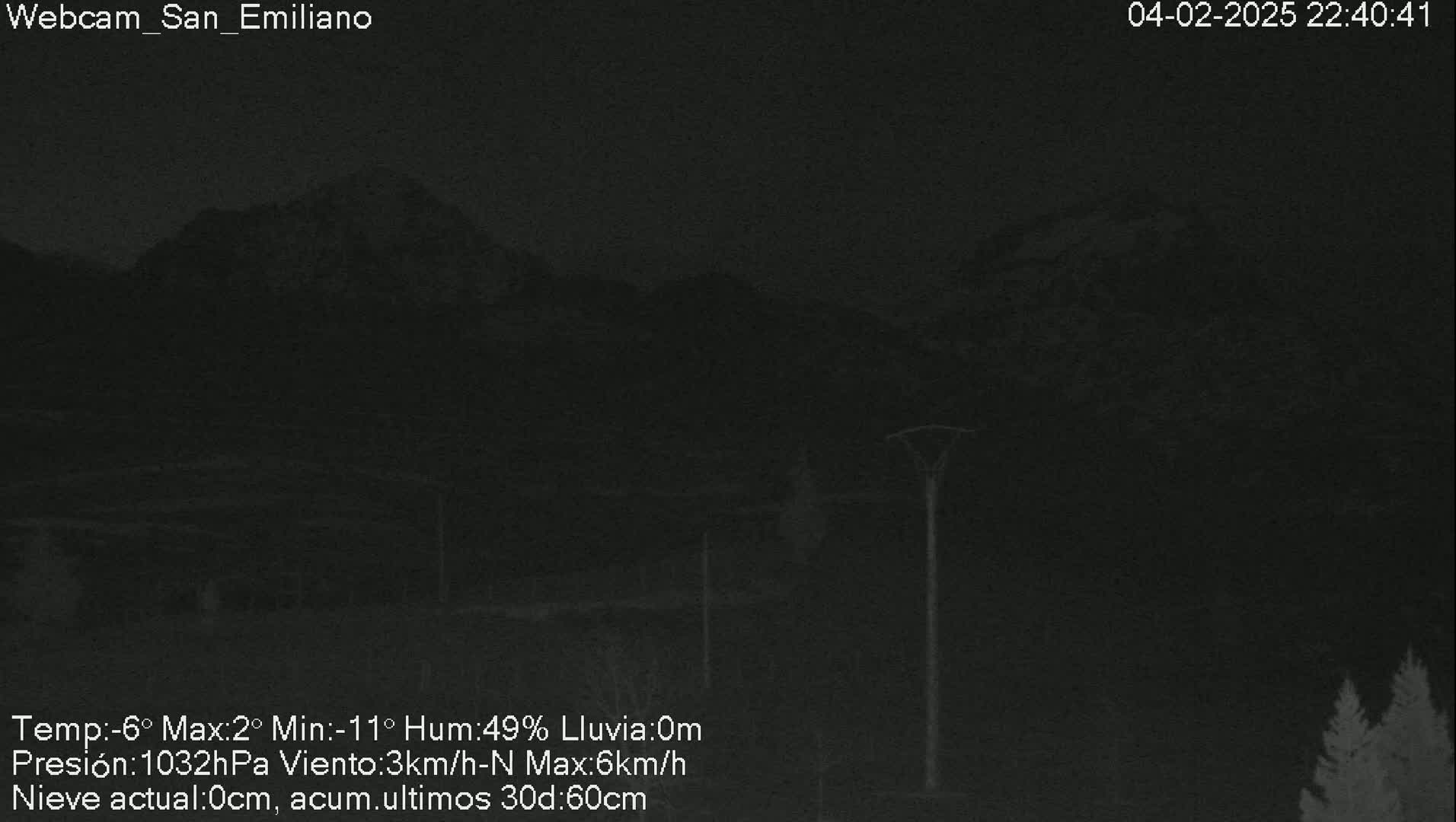 A nighttime view of dark mountains under a cloudy sky with no precipitation.