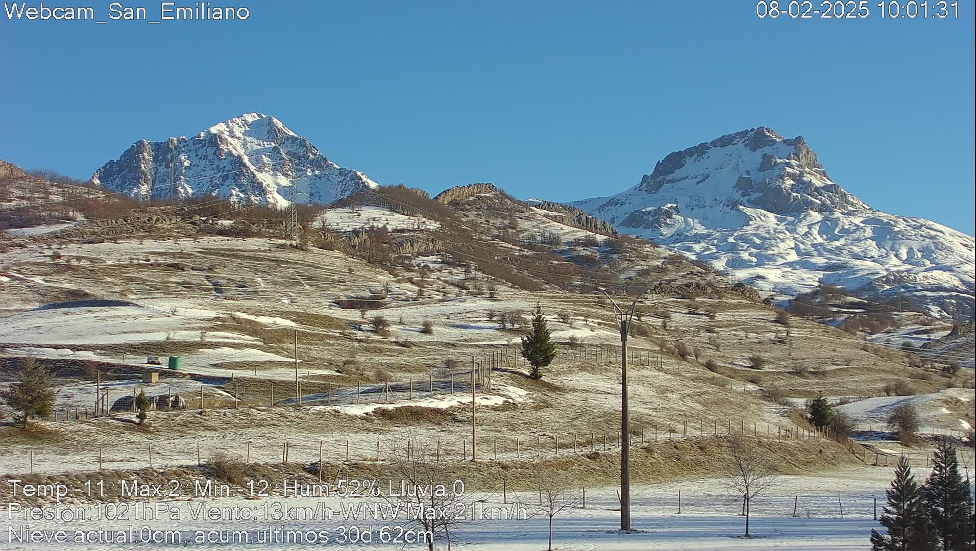 A snow-dusted landscape with two snow-capped mountains in the background under a clear blue sky.