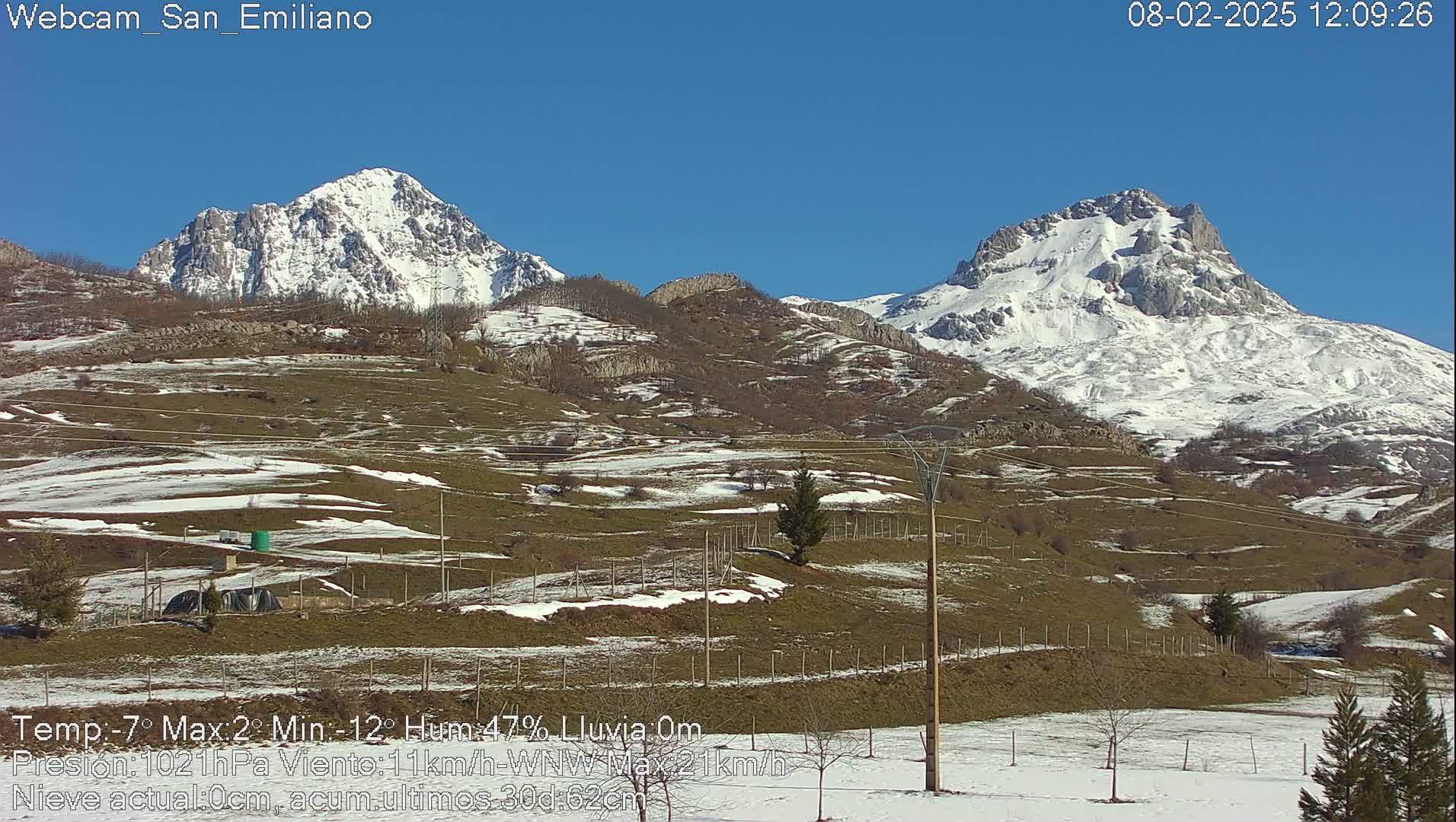 A snow-dusted mountain range is visible under a clear blue sky, with patches of snow on the lower hills in the foreground.