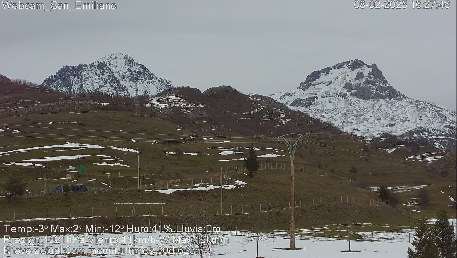 Two snow-capped mountains are visible in the distance on an overcast day, with patches of snow on the hills in the foreground.