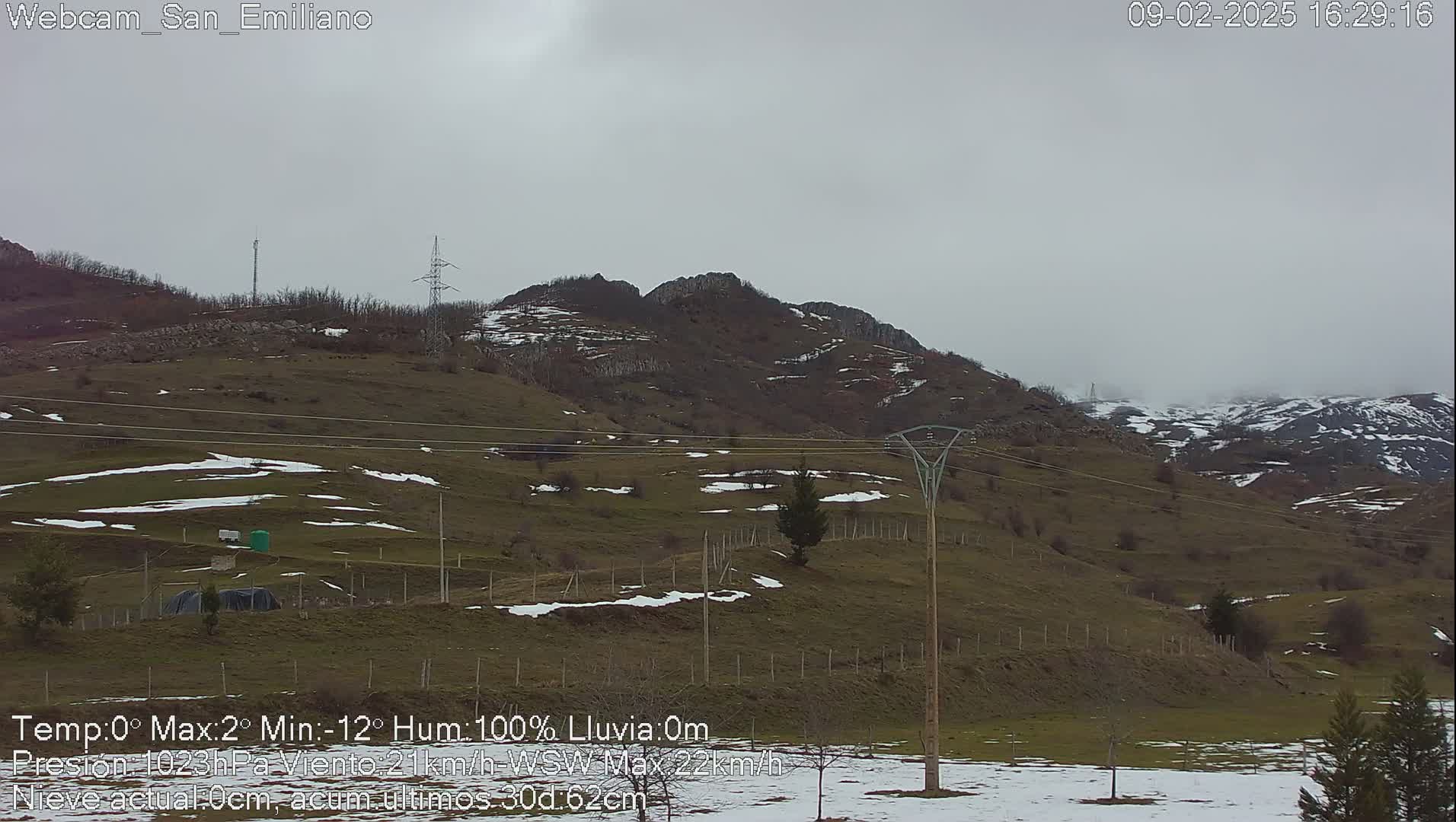 A hilly landscape with patches of snow under an overcast sky.