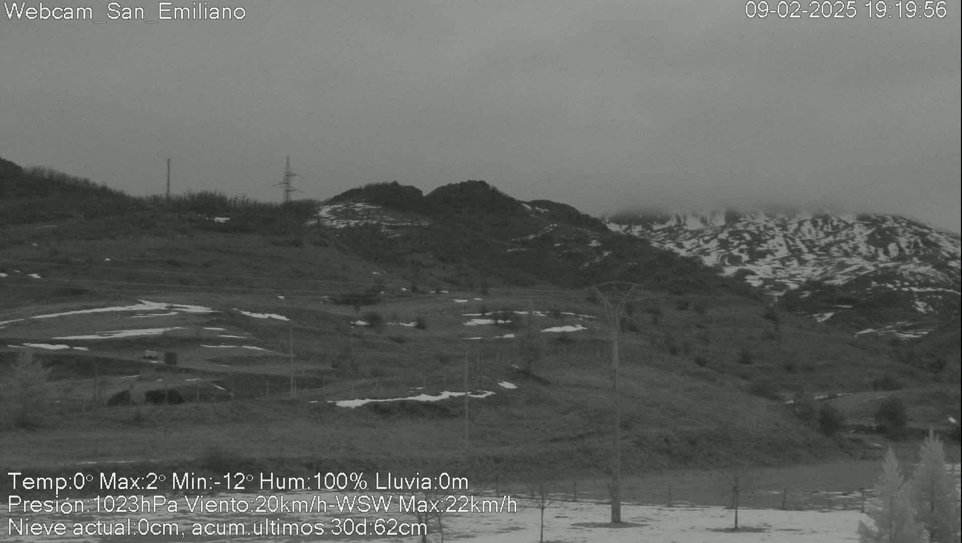 A foggy, snow-dusted mountain range is seen in the distance, with a sparsely vegetated foreground showing patches of snow.