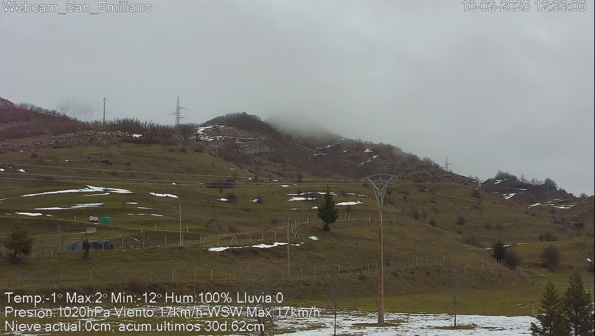 A foggy, overcast day reveals a sparsely vegetated hillside with patches of snow, power lines, and a few scattered trees.