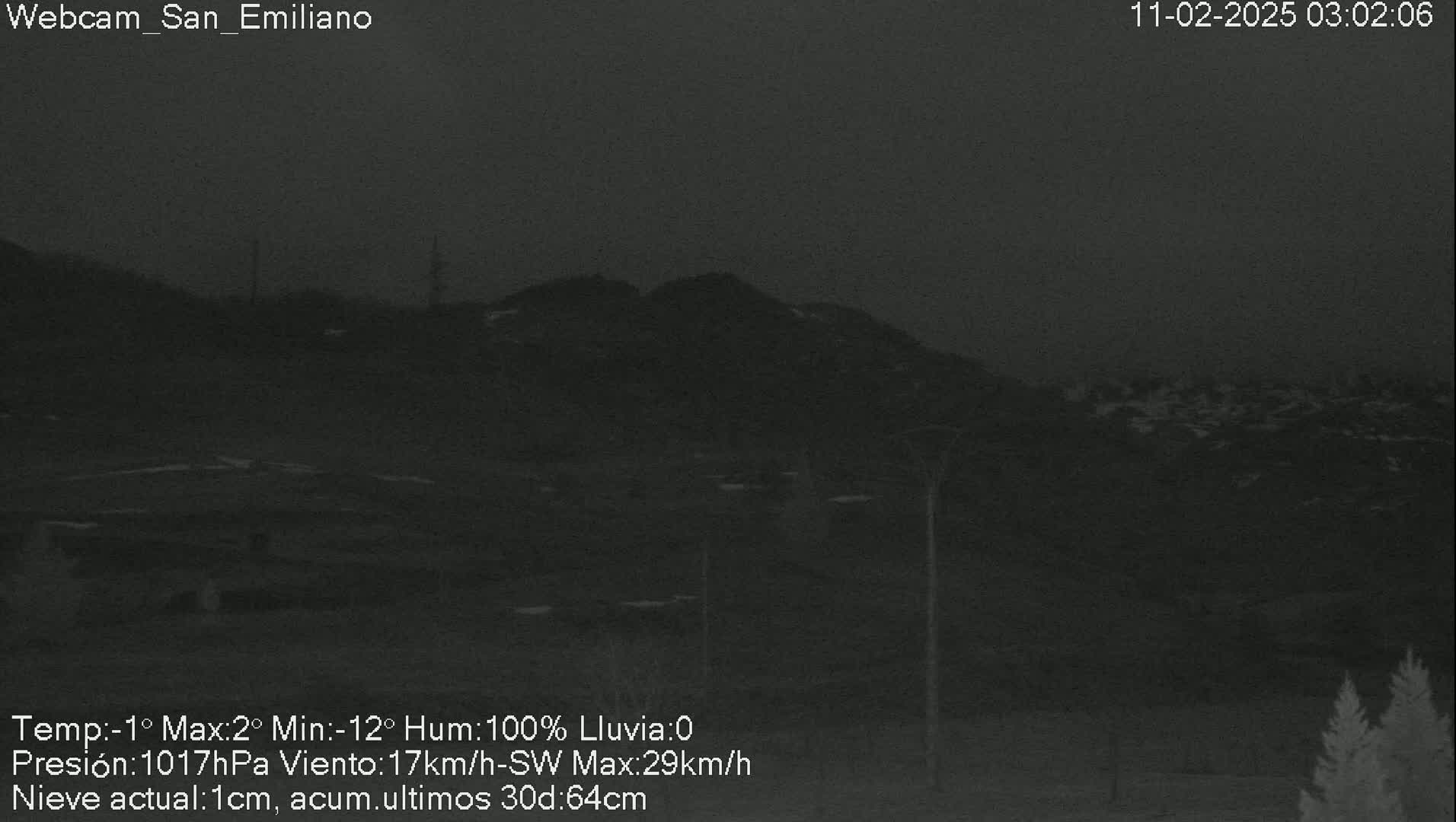 A dark, nighttime view of a snow-covered hill under a cloudy sky.