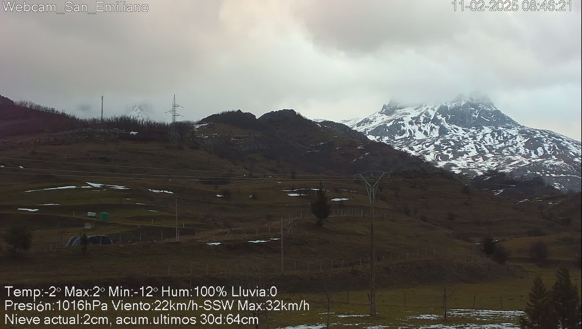 A snow-dusted mountain range is visible under an overcast sky, with a field in the foreground showing patches of snow.
