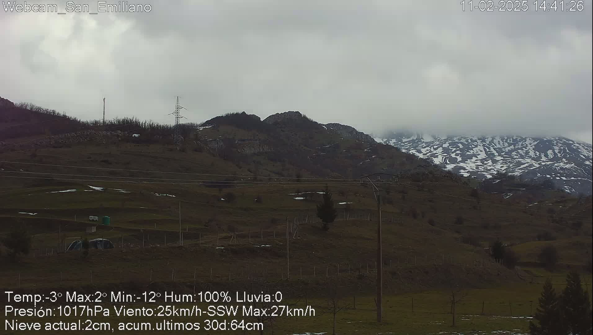 A mostly cloudy, overcast day reveals snow-dusted mountains in the distance, with a low-lying, sparsely vegetated valley in the foreground.