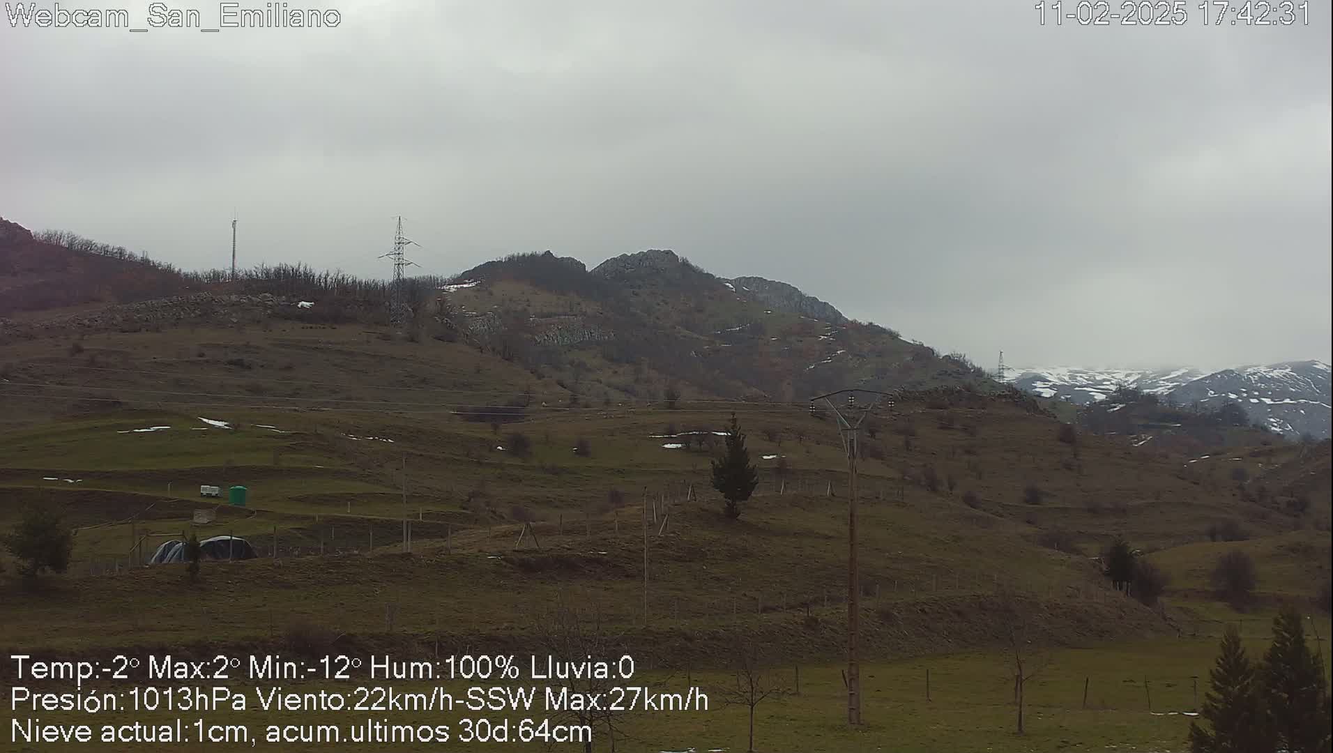 A view of brown, rolling hills under an overcast sky, with some snow visible on distant mountains.