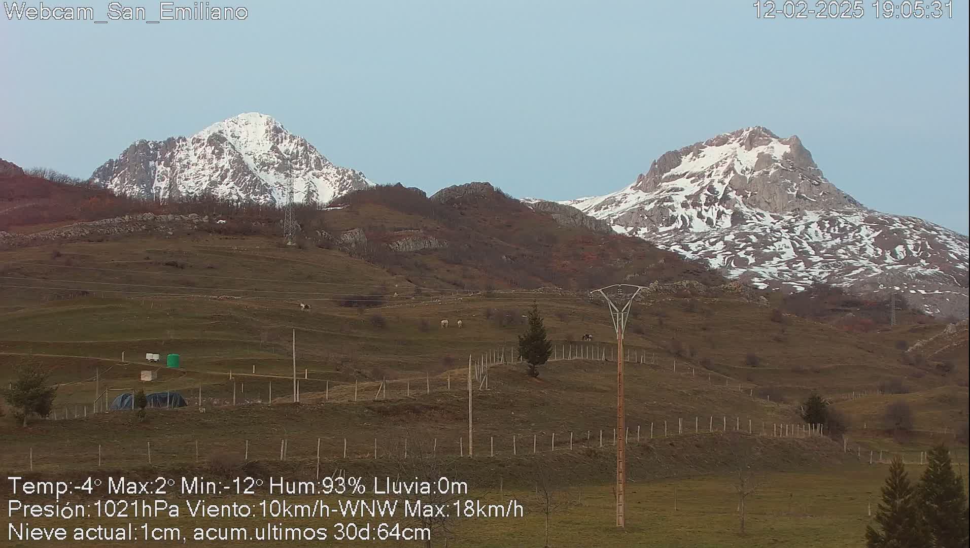 Two snow-capped mountains rise in the distance above a brown and green hillside under a clear, pale sky.