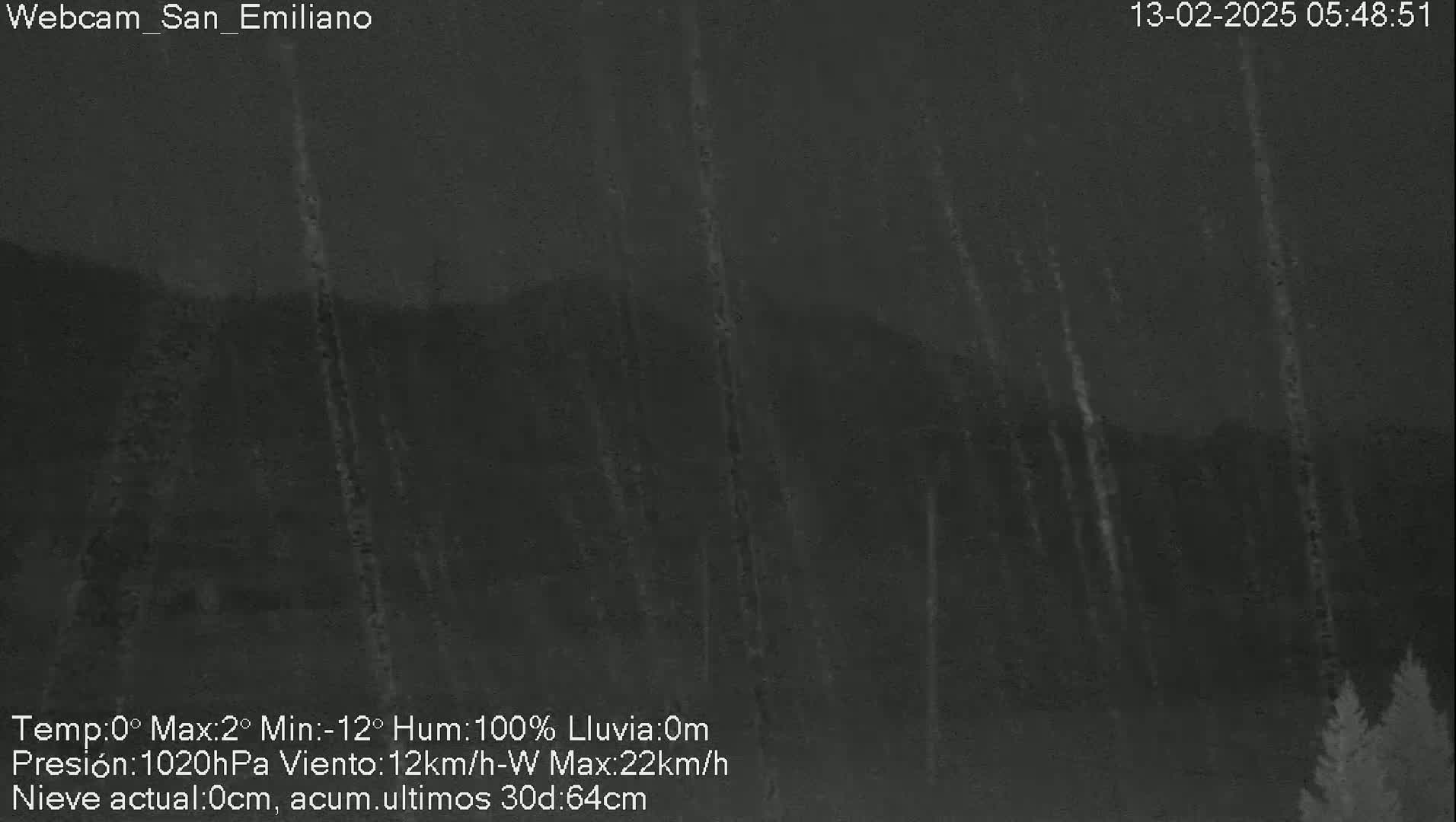 A nighttime, outdoor scene shows heavy rain falling in front of a dark mountain range with some trees visible in the bottom right corner.