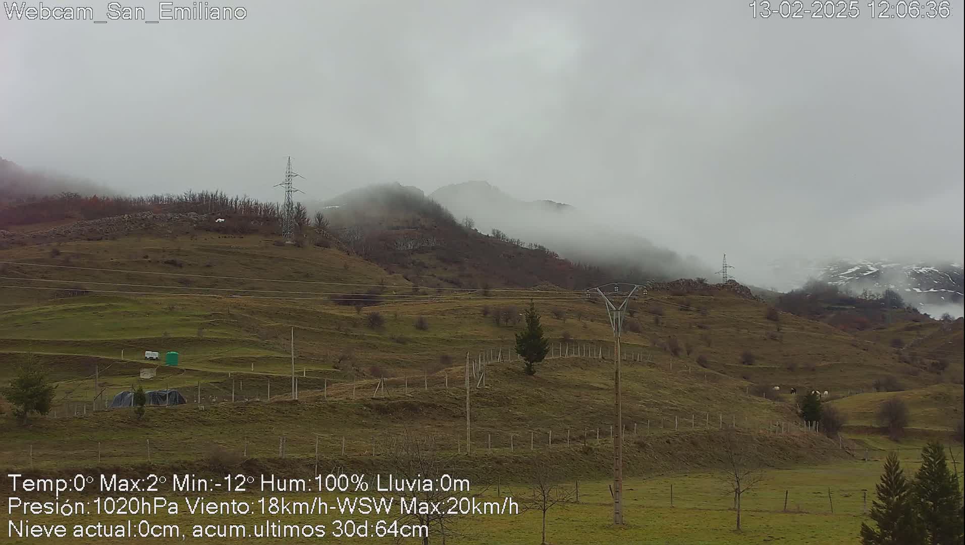 A foggy, overcast day reveals rolling green hills dotted with sparse trees and a few structures, with mountains shrouded in mist in the background.