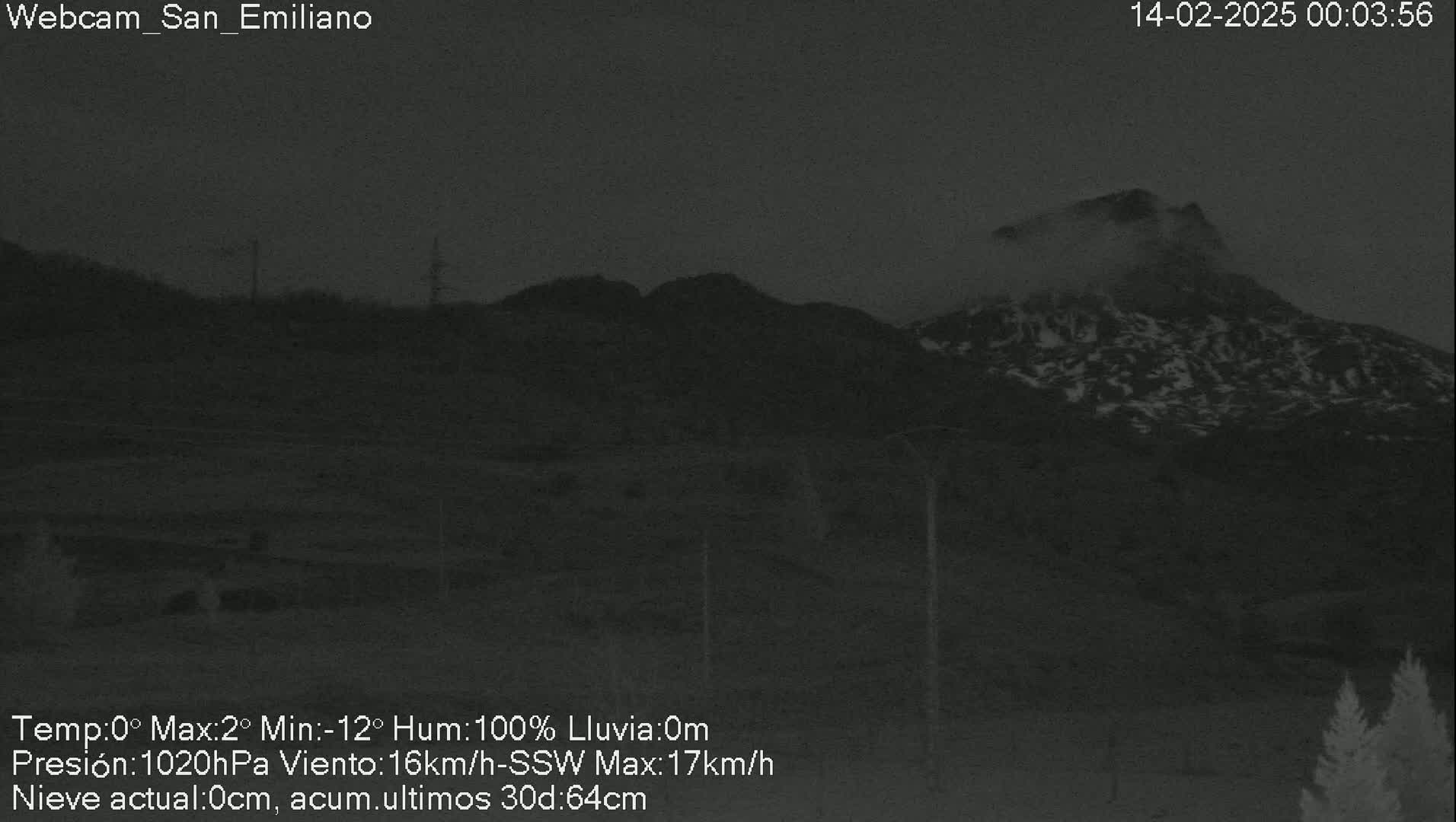 A nighttime, low-visibility view of snow-dusted mountains shrouded in fog or mist.