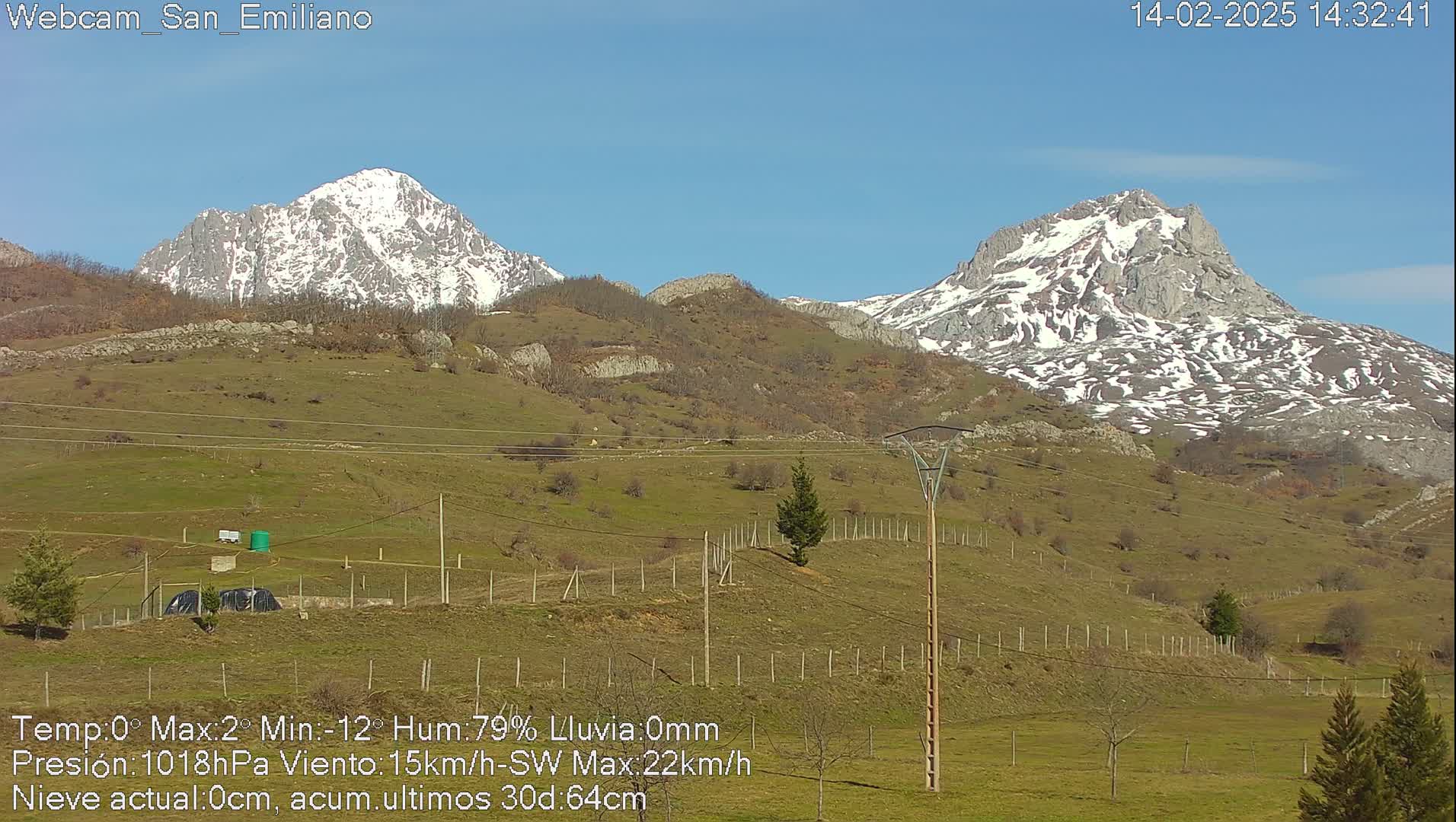 Two snow-capped mountains are visible in the distance, overlooking a grassy hillside under a clear blue sky.