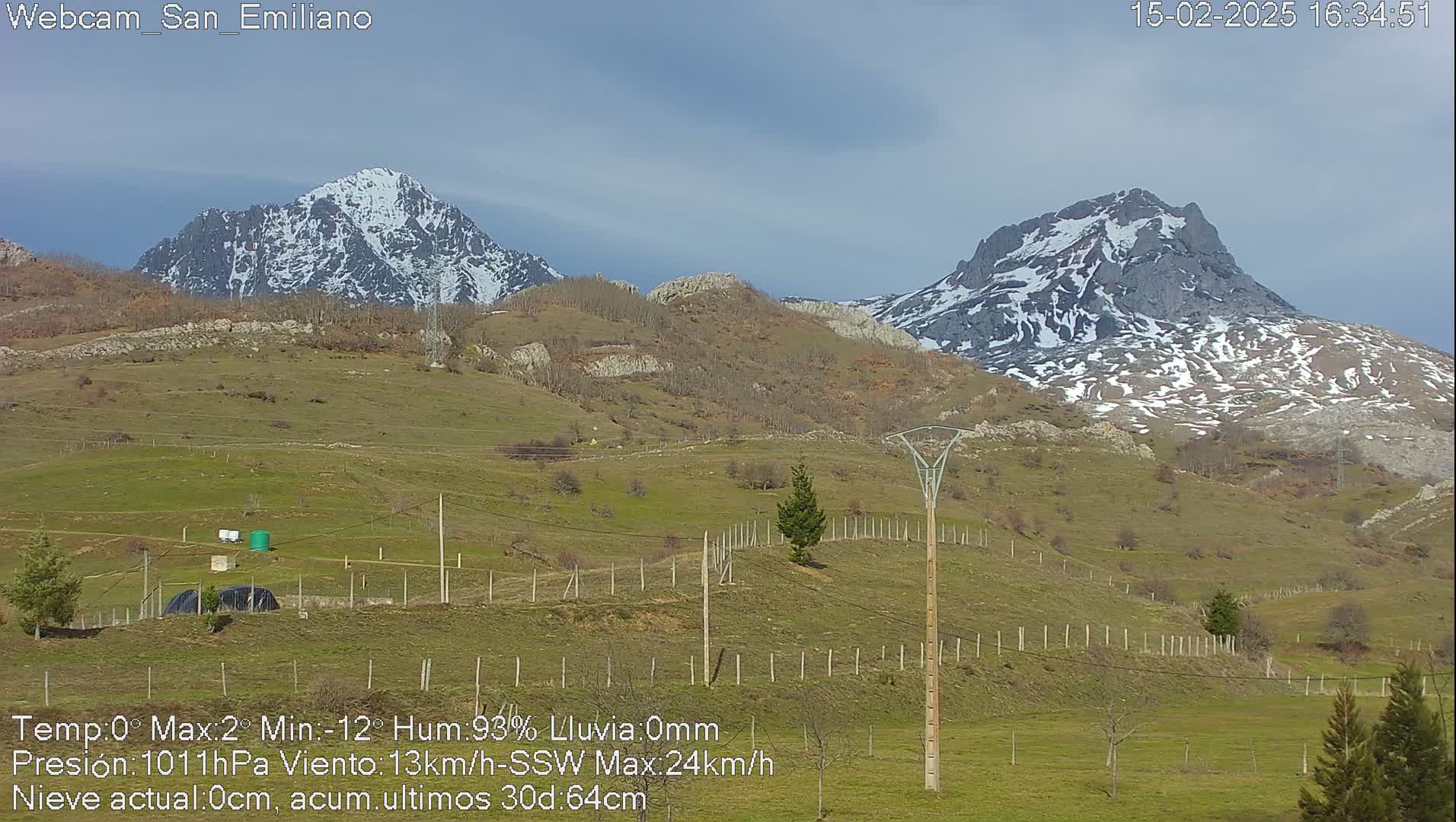 Two snow-capped mountains rise in the distance behind a gently sloping green hillside under a mostly cloudy sky.