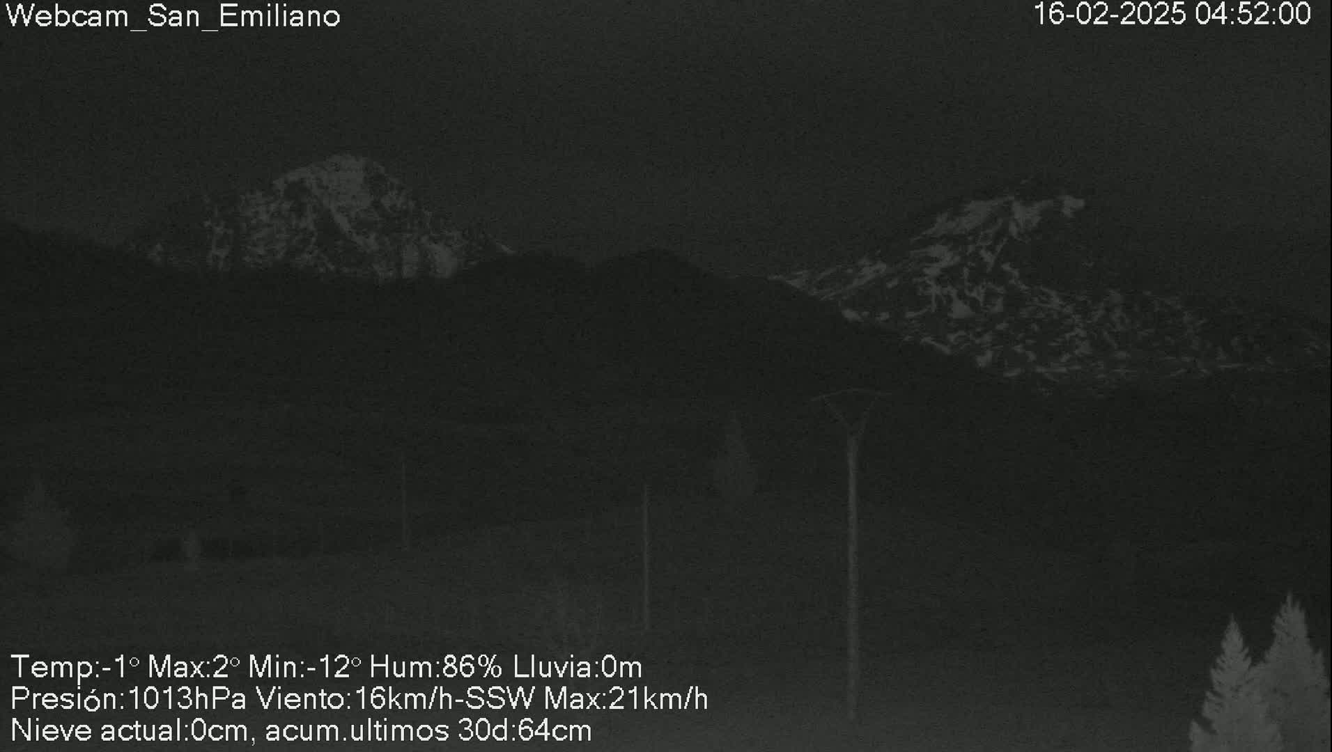 A nighttime, low-light view of snow-capped mountains under a dark sky with rain.