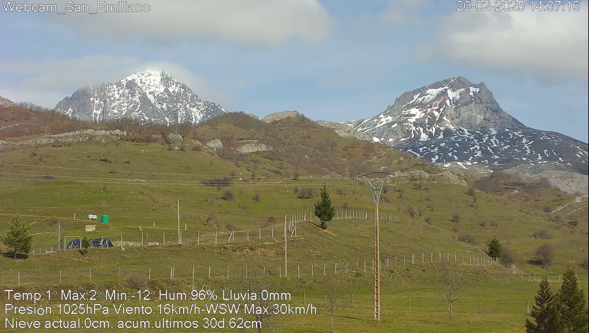 Two snow-capped mountains rise in the distance above a grassy hillside under a partly cloudy sky.