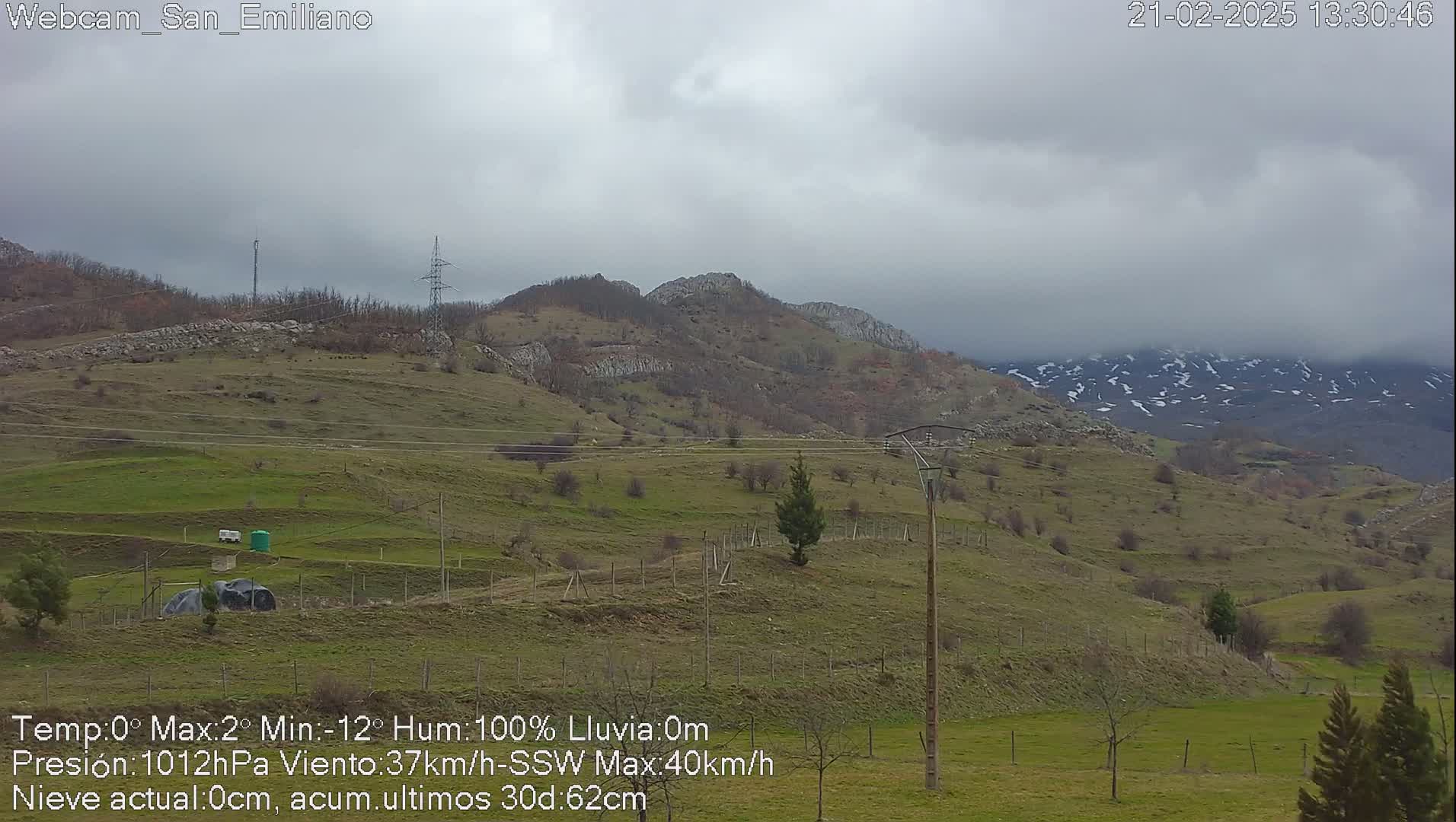 A view of a hilly landscape under an overcast sky, with some snow visible on distant mountains.