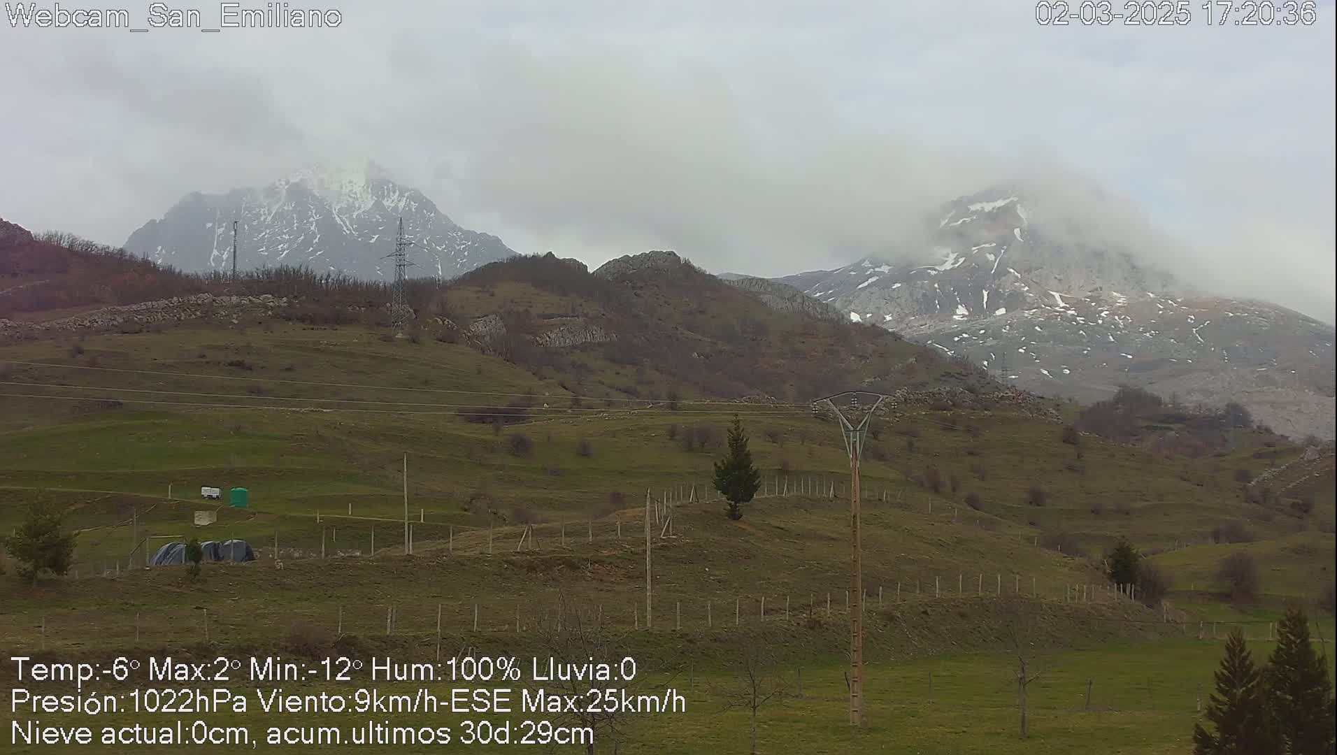 A misty, overcast day reveals snow-capped mountains in the distance, overlooking a hilly landscape with sparse vegetation.