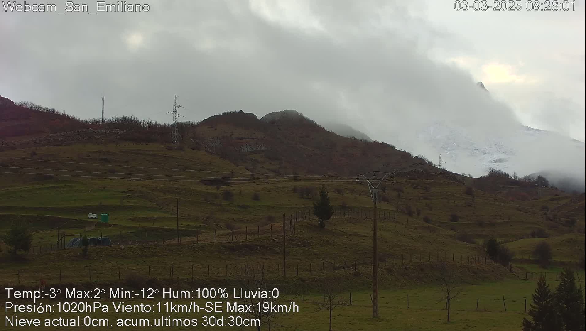 A foggy, overcast day reveals rolling green hills and a snow-capped mountain peak in the distance, with power lines cutting across the landscape.