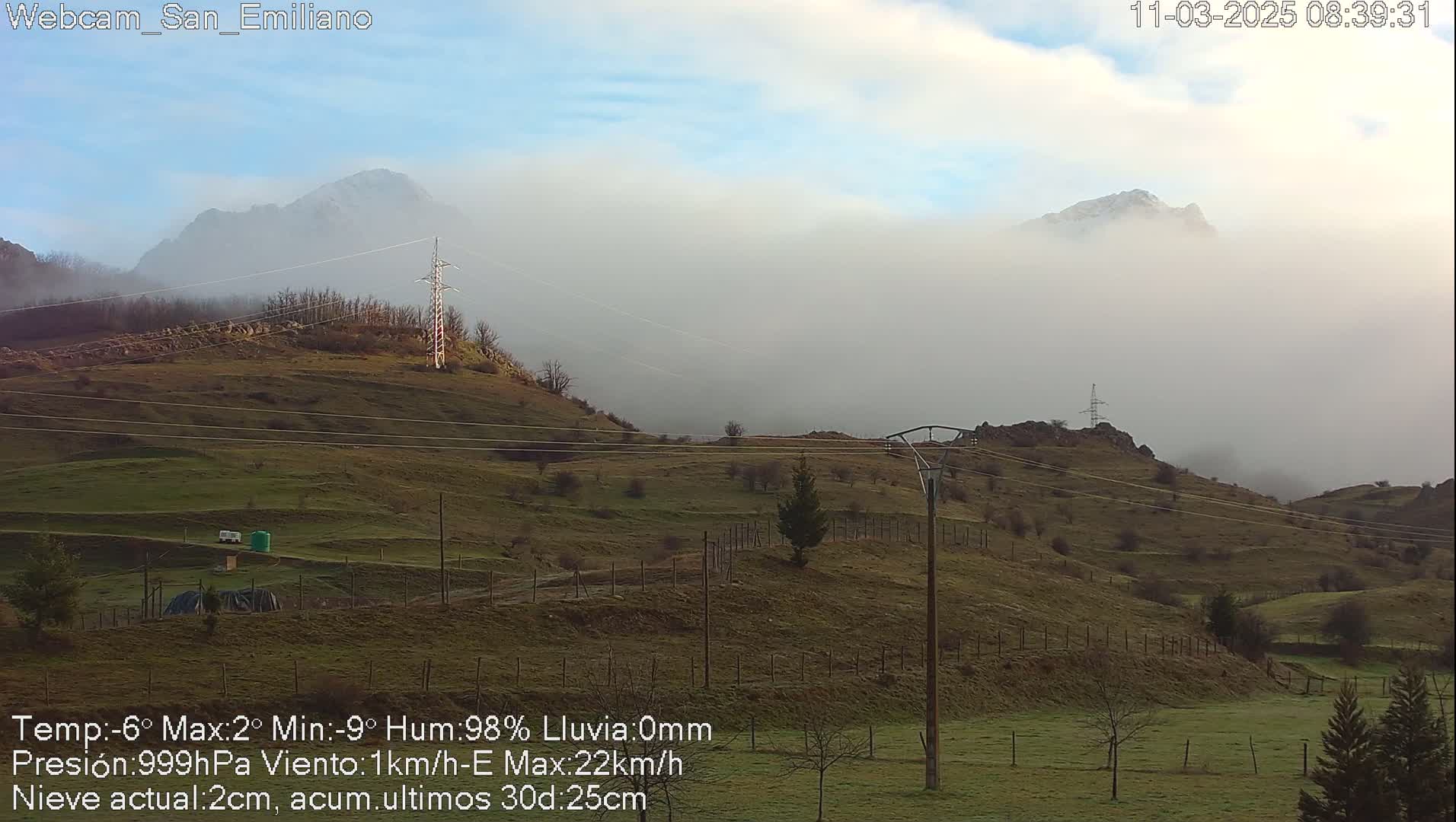 A misty, hilly landscape with power lines stretches towards mountains shrouded in fog under a mostly clear sky.