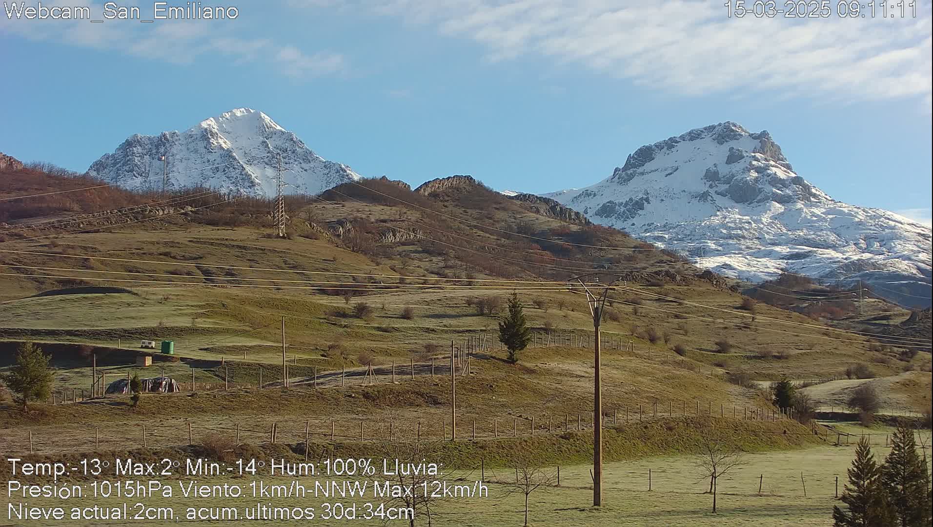 Two snow-capped mountains rise in the distance behind a frost-covered field, under a mostly clear sky.