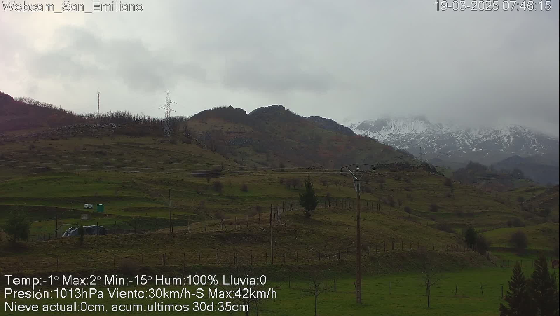 A view of rolling green hills and distant snow-capped mountains under a cloudy, overcast sky.