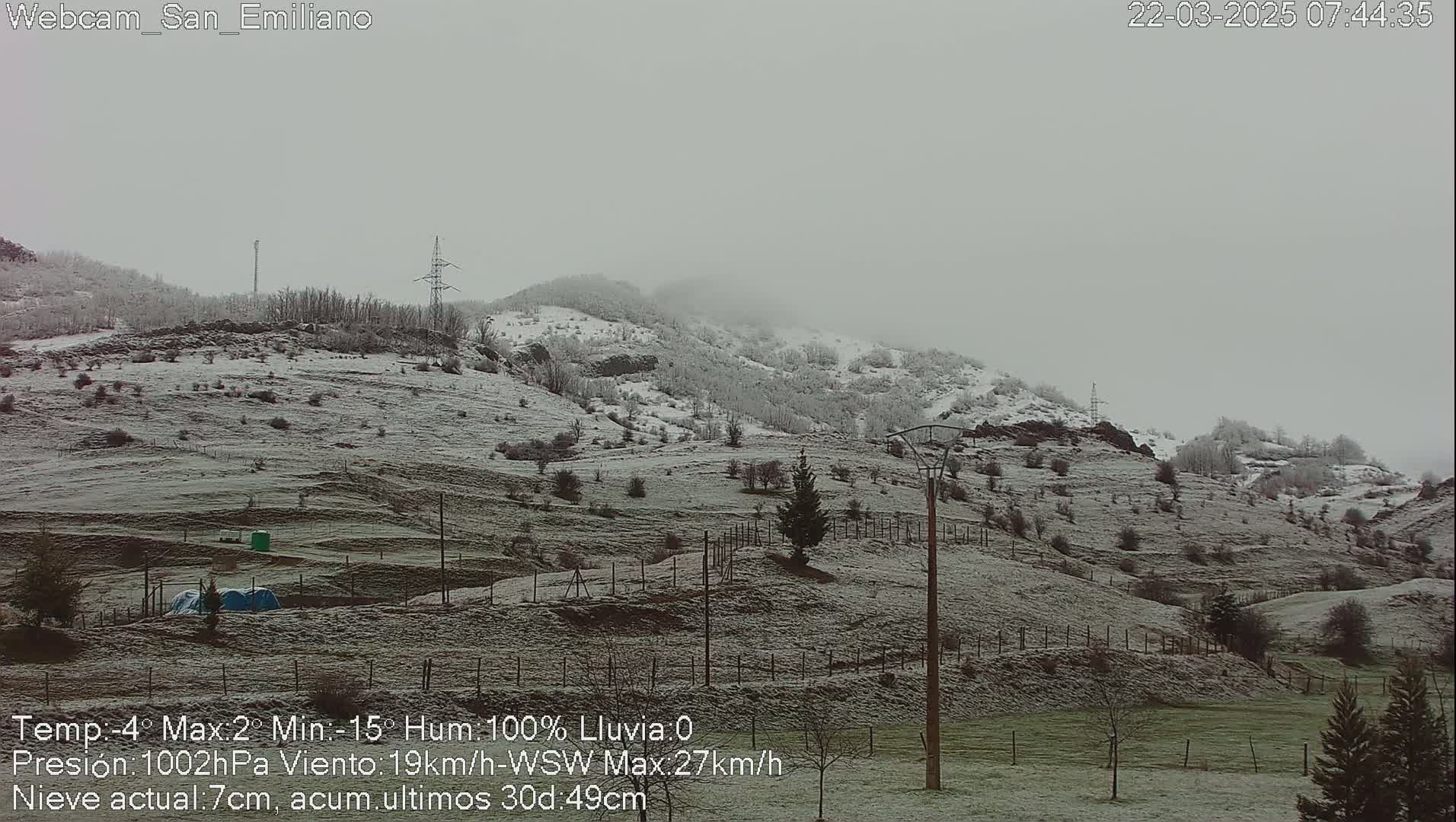 A snow-covered landscape of rolling hills and sparsely wooded areas under an overcast sky.