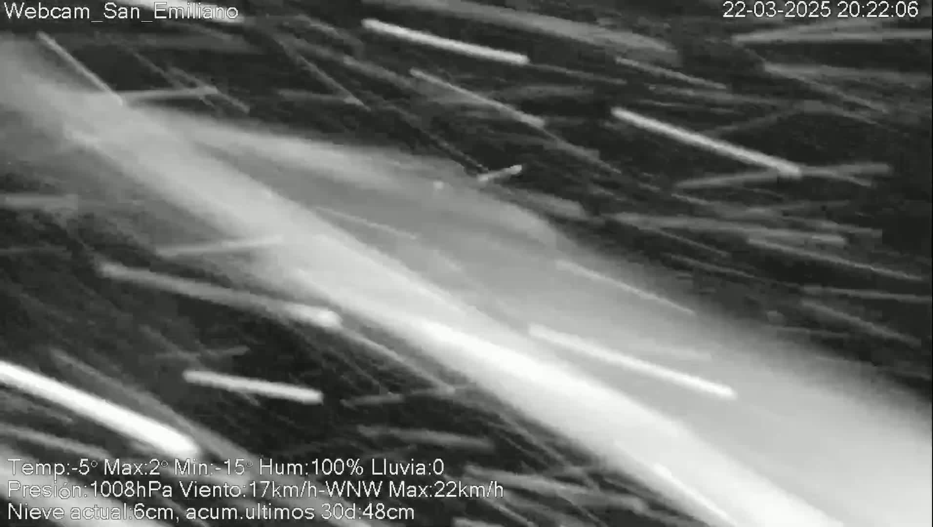 A grainy, black and white image shows heavy snowfall with streaks of white against a dark background.