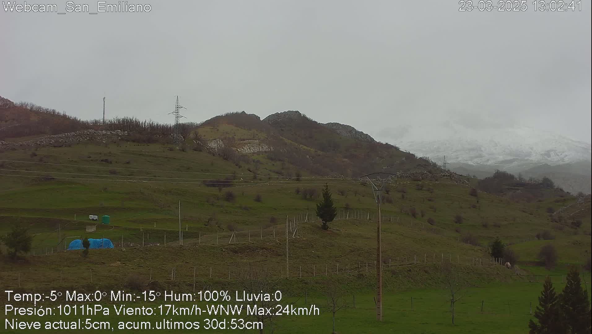 A view of a hilly landscape under an overcast sky, with some snow visible on distant mountains.