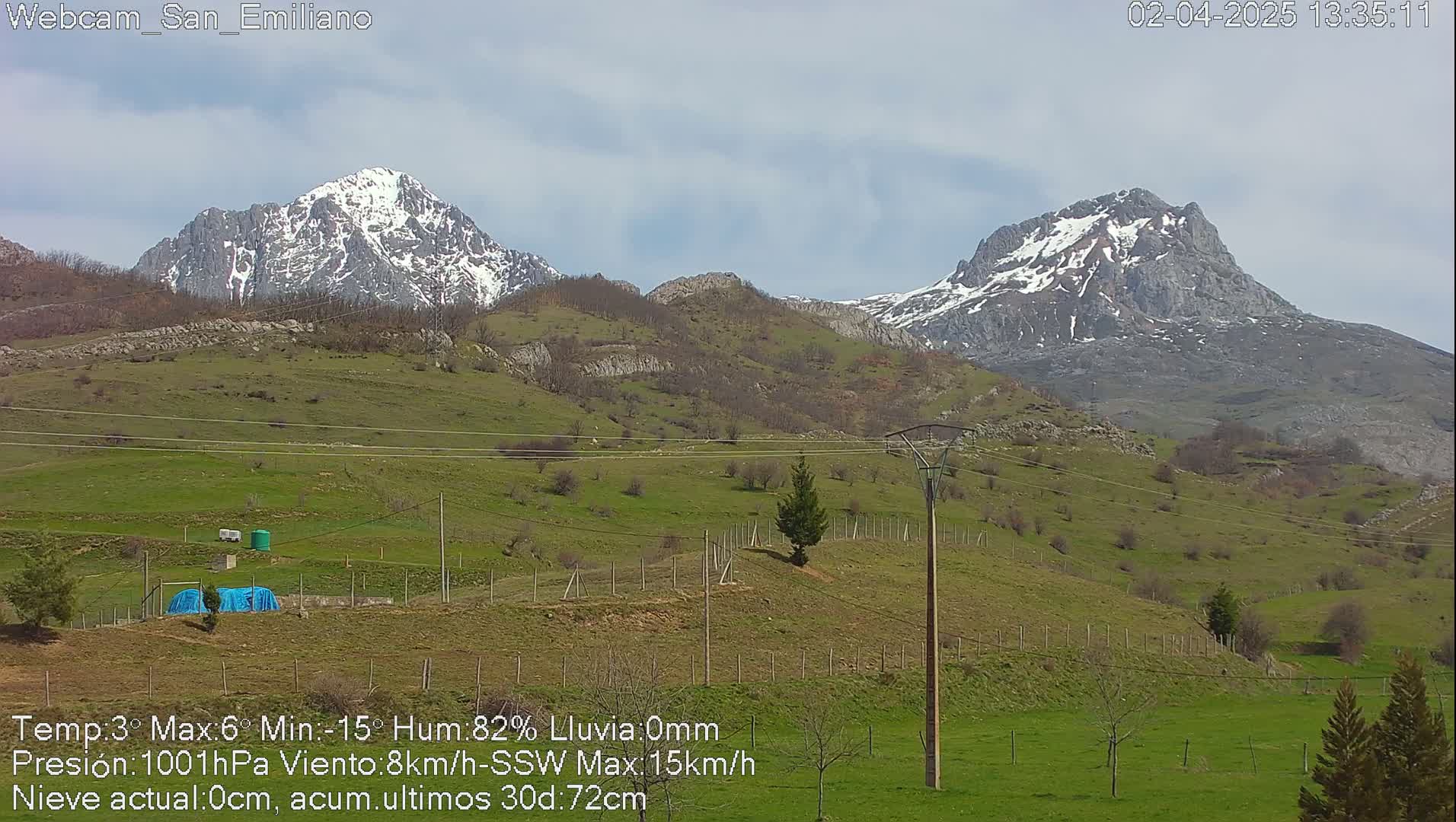 Two snow-capped mountains rise in the distance behind a grassy hillside under a partly cloudy sky.